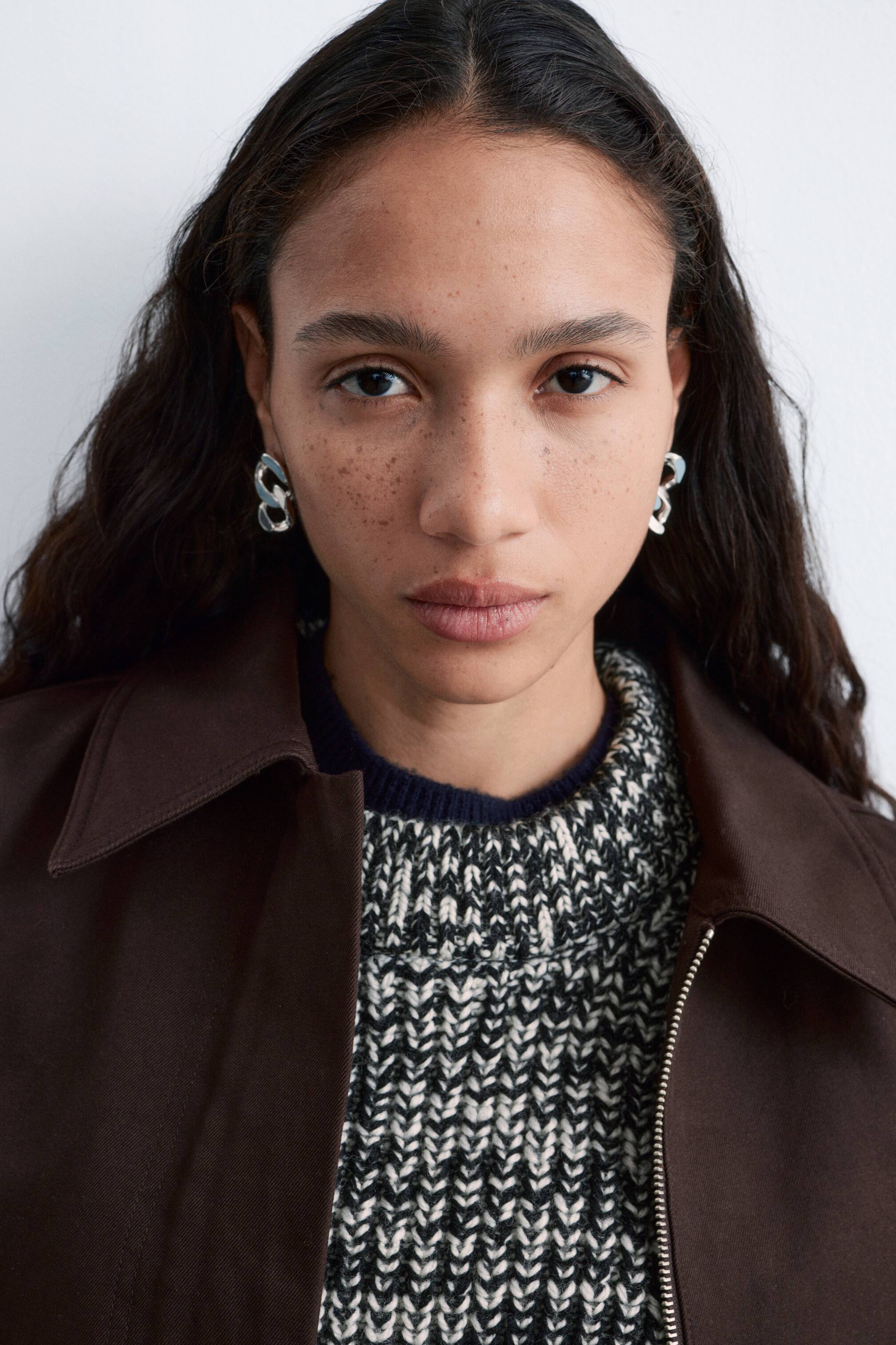 Agrandir l'image: Boucles d'oreilles sculpturales ton argent, ornées de deux maillons de chaîne gourmette entrelacés, portées par le mannequin sur les deux oreilles.