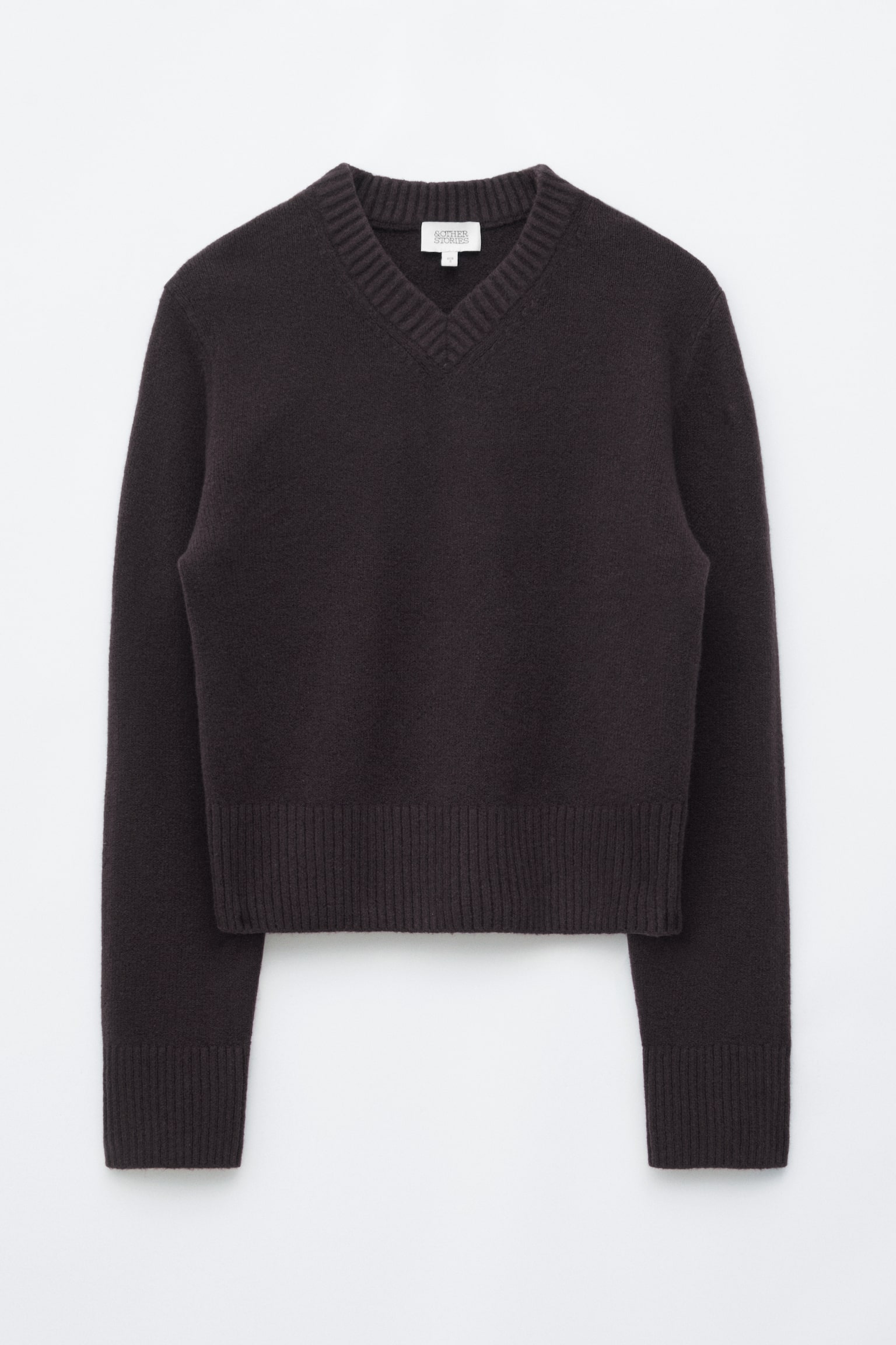 Un maglione lavorato a maglia marrone scuro è mostrato frontalmente, caratterizzato da un ampio scollo a V a coste e una silhouette dalla vestibilità regolare. Presenta un ampio bordo a coste e polsini coordinati a coste sulle maniche lunghe.