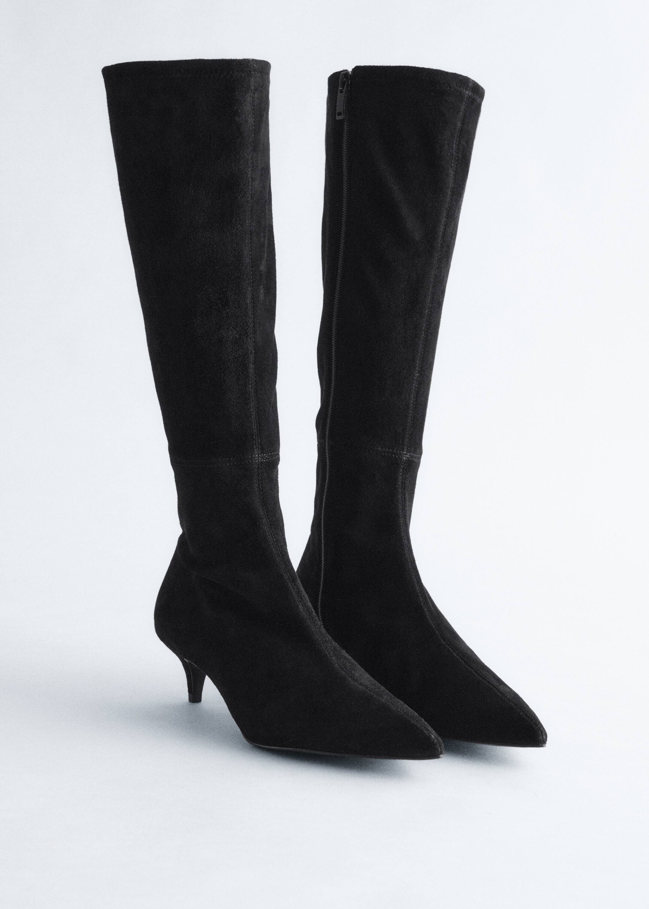 Visa större bild: Ett par svarta knähöga stövlar, tillverkade av slät stretchmocka, är placerade med framsidan framåt. De har en elegant, spetsig tå och en smal kittenklack, med en dragkedja i full längd synlig längs insidan av den högra stövelns skaft.