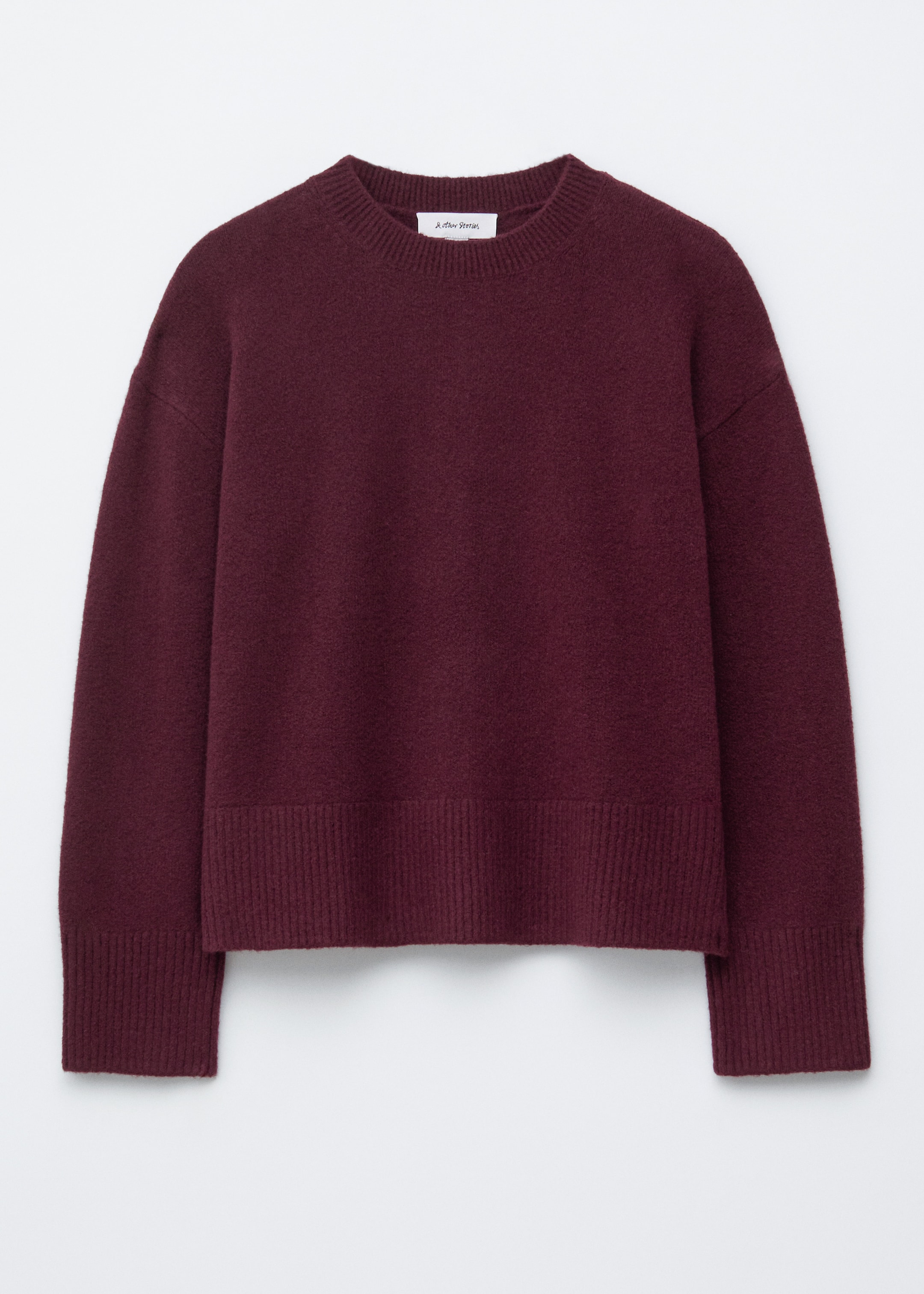 Grösseres Bild ansehen: Ein dunkelroter Strickpullover mit langen Ärmeln wird von vorne gezeigt und zeichnet sich durch eine entspannte Silhouette aus. Er ist mit einem gerippten Ausschnitt, gerippten Bündchen und einem gerippten Saum versehen.