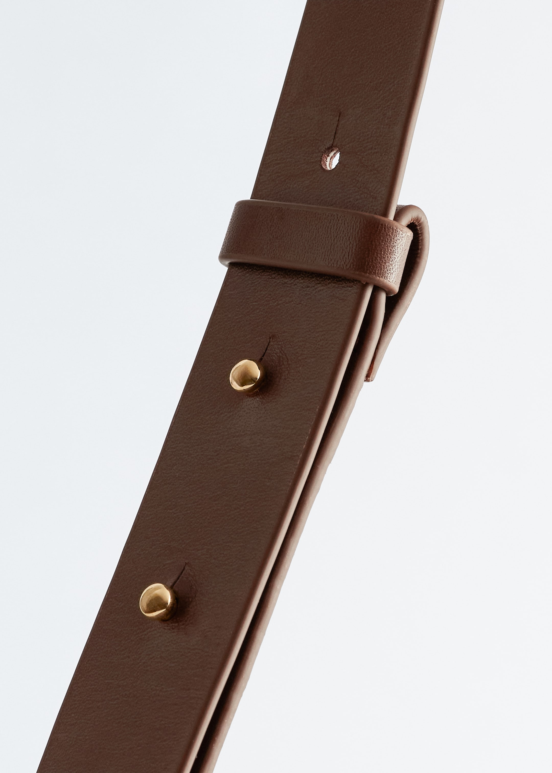 View larger image: The brown leather shoulder strap is showing two gold-tone studs, a strap keeper, and an adjustment hole.