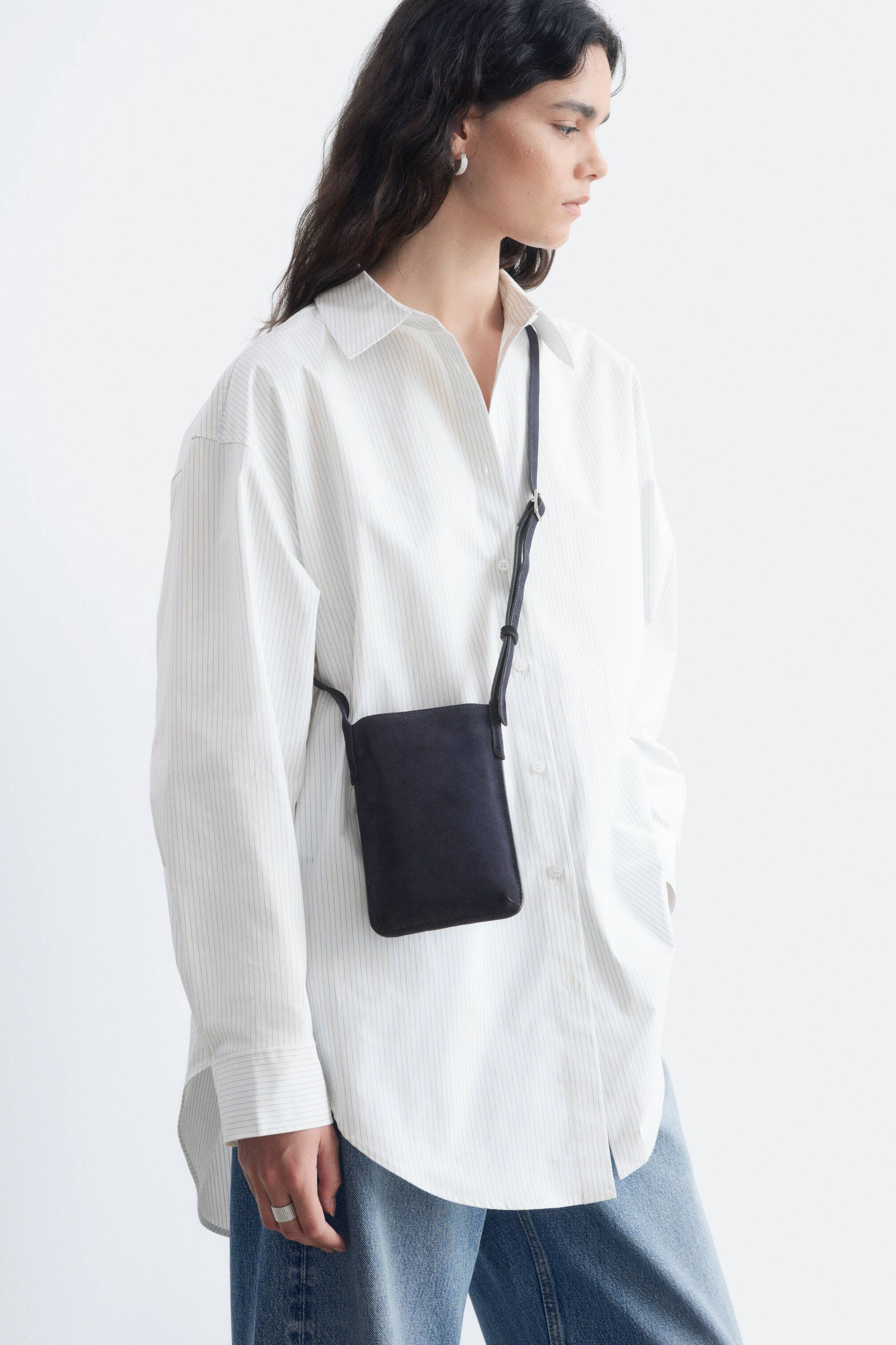 View larger image: A small, dark blue rectangular crossbody bag with a suede-like texture and a thin, adjustable strap featuring a silver buckle is worn across a person’s torso, facing forwards.