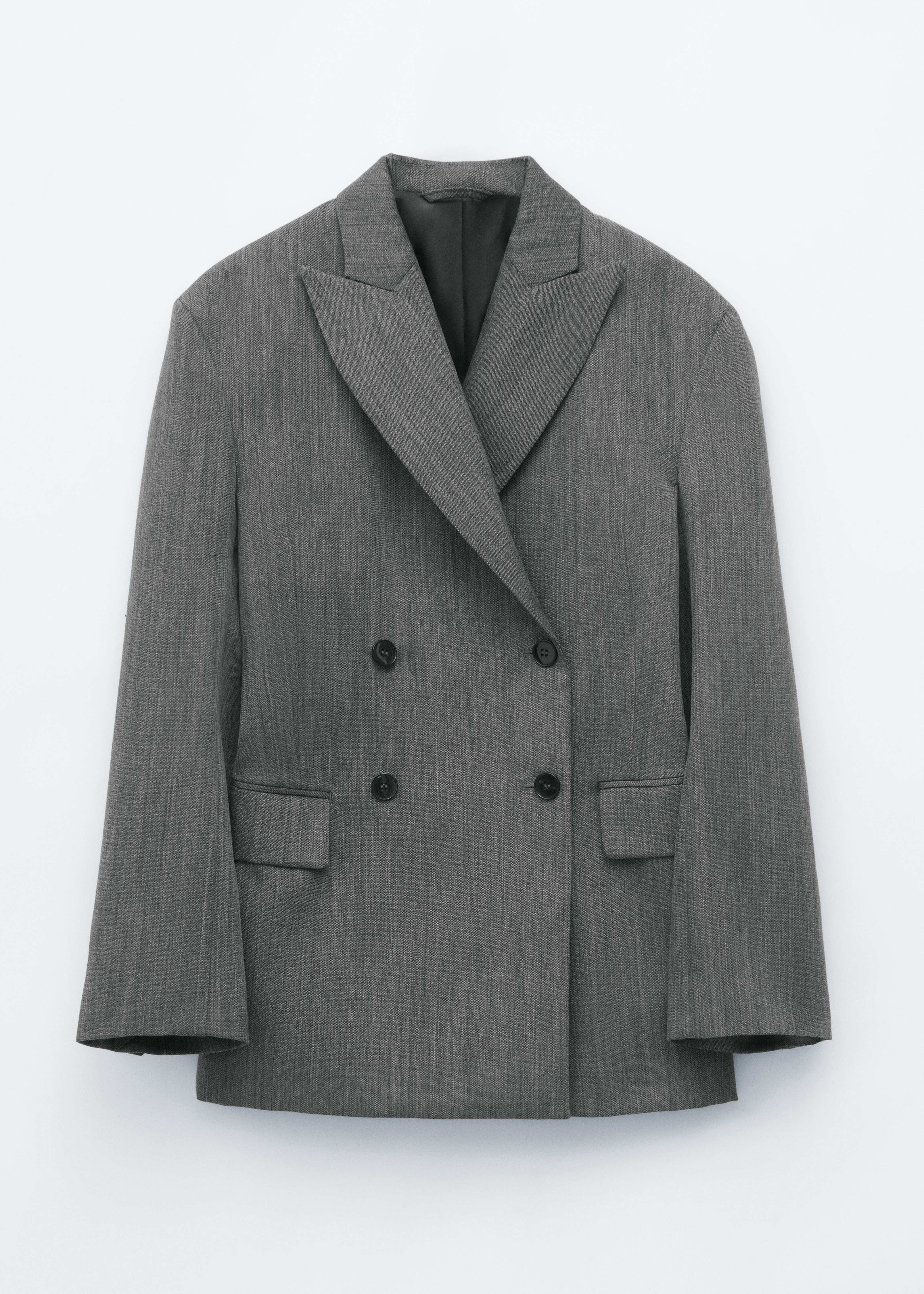 Una blazer grigio a doppiopetto con rever a lancia e vestibilitÃ  rilassata Ã¨ indossata dalla modella sopra un top grigio e jeans blu. La blazer Ã¨ abbinata a una sciarpa fantasia drappeggiata intorno al collo e a una borsa intrecciata nera.