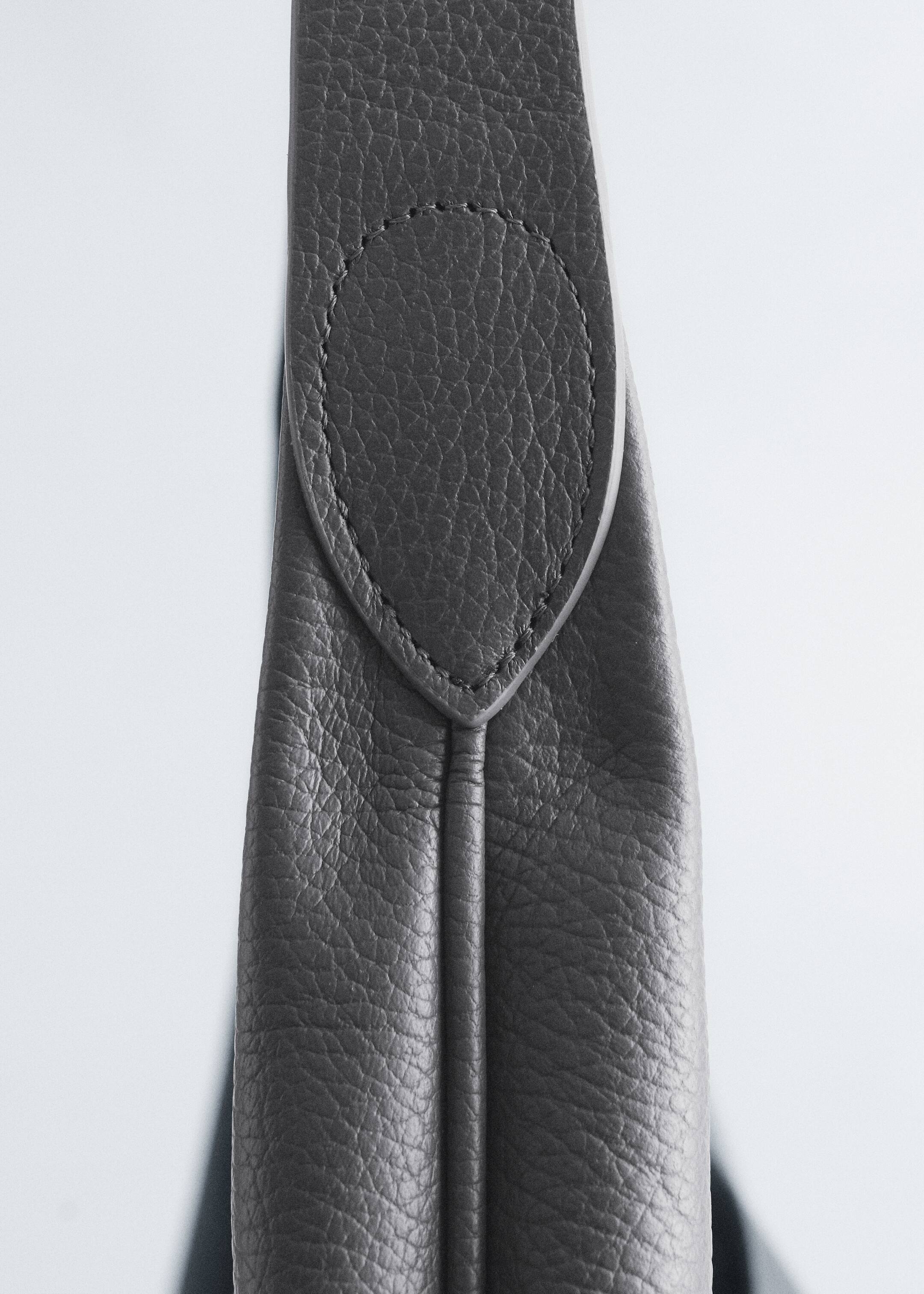 Agrandir l'image: Une sangle en cuir gris foncé à texture granuleuse présente une superposition de forme ovale, fixée avec des surpiqûres assorties, sur le dessus. Une couture verticale distincte descend au centre de la sangle sous la superposition.