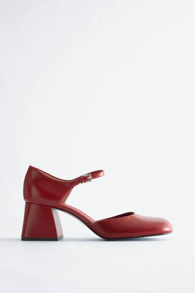 A red leather Mary Jane pump is facing side, showcasing a square toe, a chunky block heel, and a strap with a silver buckle. - 1