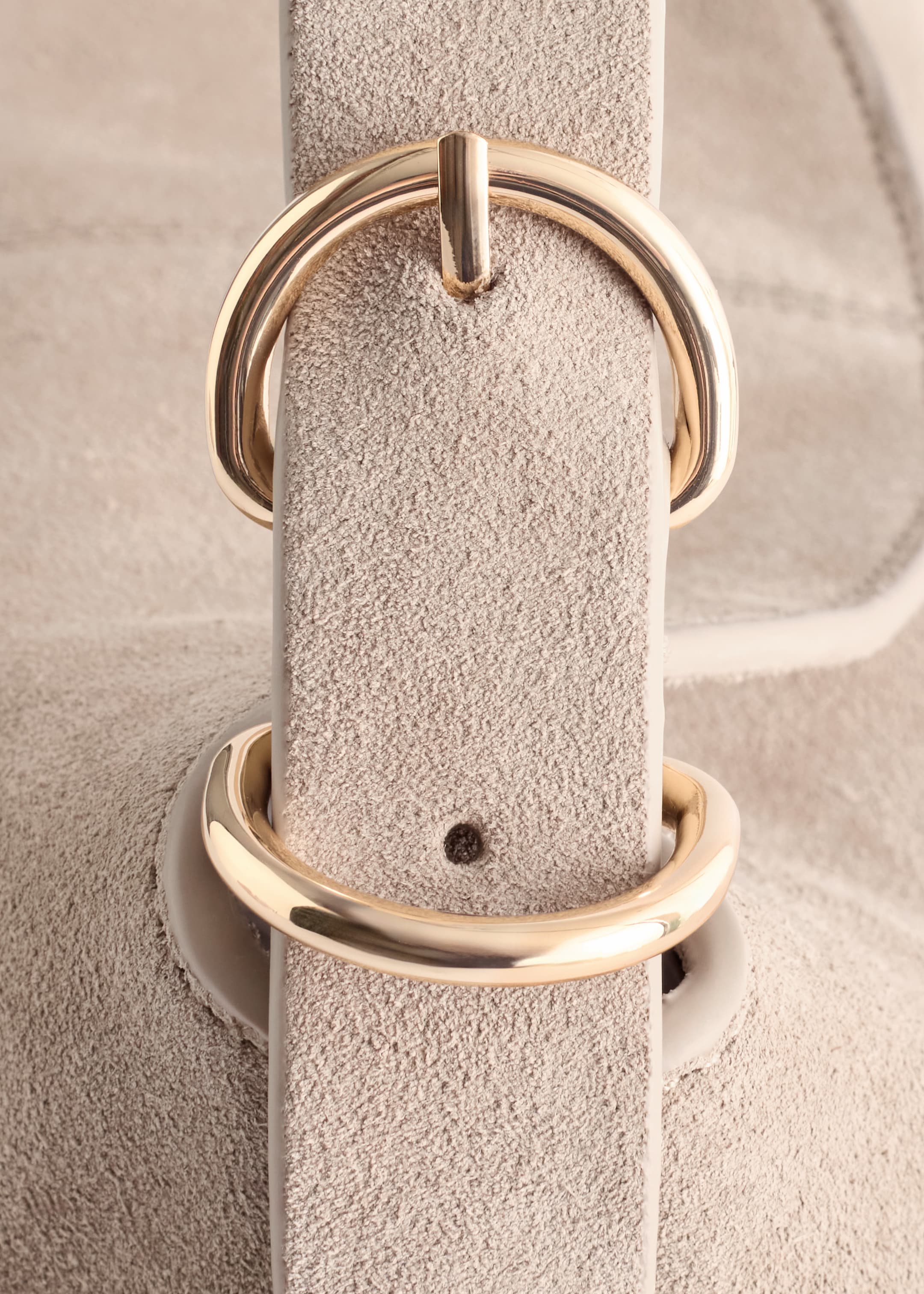 Agrandir l'image: Un gros plan montre une sangle de type daim beige clair en train d'être passée à travers une boucle en D de couleur dorée brillante, avec un trou visible dans la sangle.