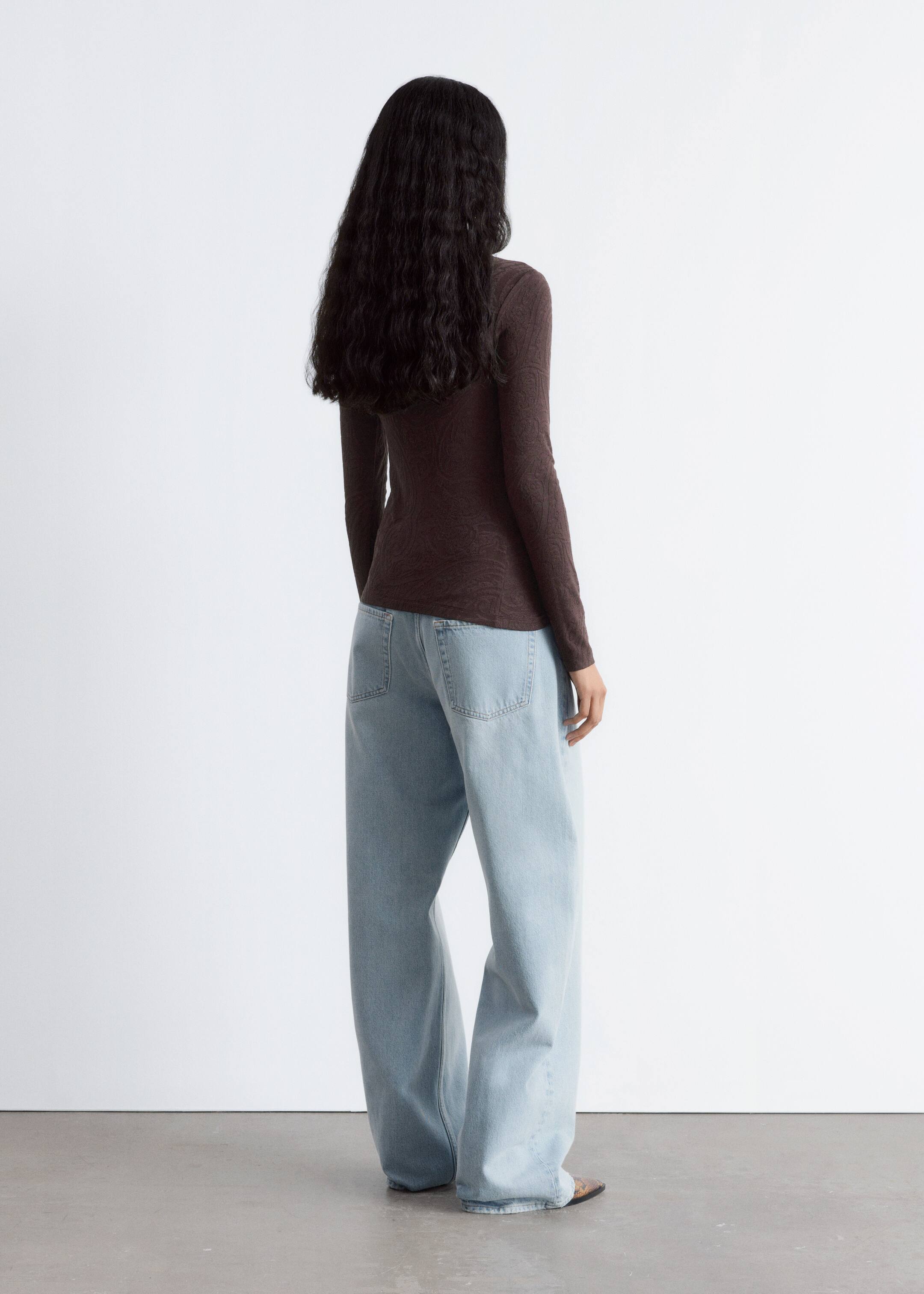 Visualizza immagine più grande: Un top a maniche lunghe di colore marrone scuro con un motivo sottile su tutta la superficie viene mostrato dal retro, mettendo in evidenza la sua silhouette aderente. Viene abbinato a jeans blu chiaro a gamba larga con tasche posteriori visibili e una vestibilità rilassata.