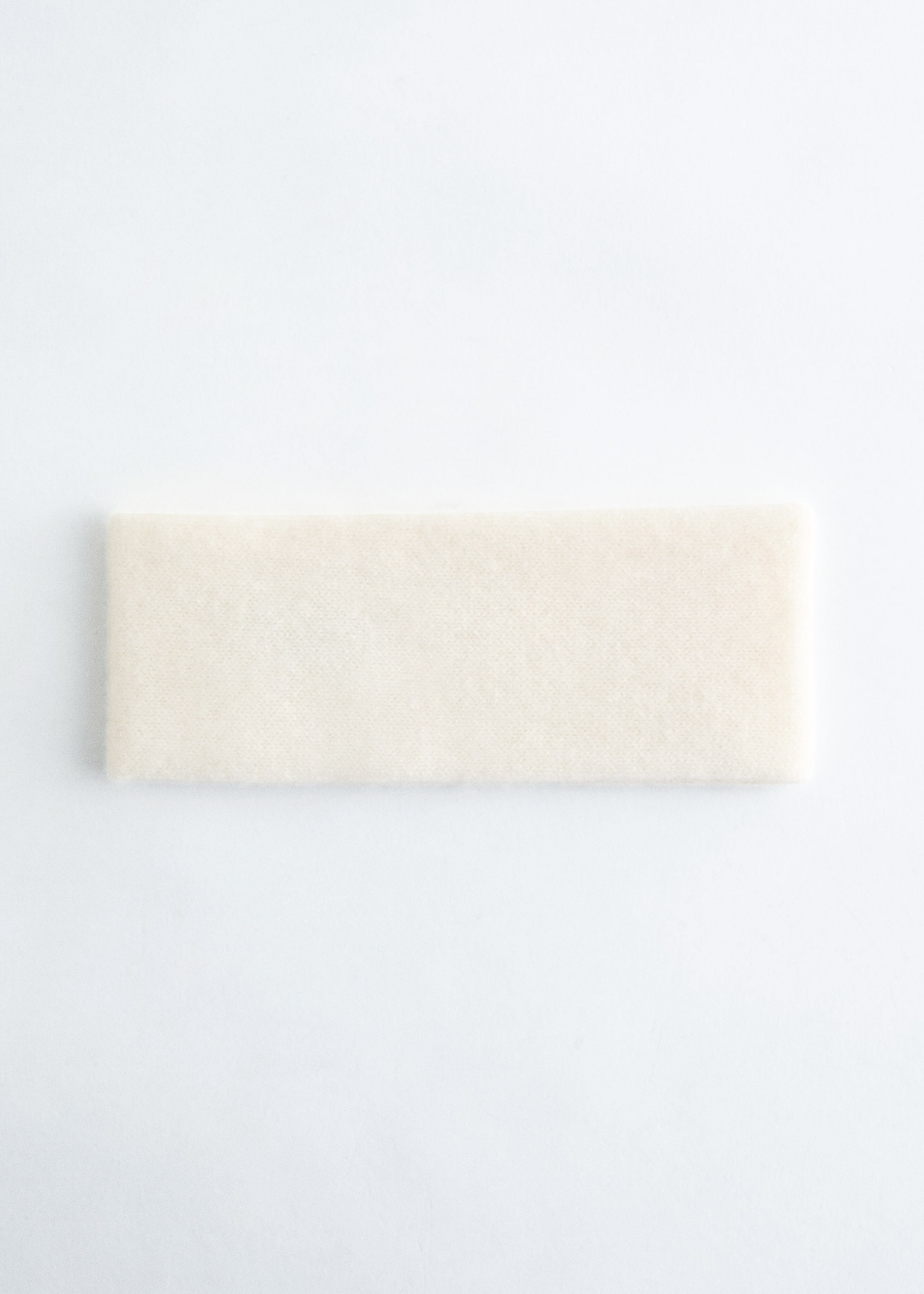 Agrandir l'image: Un bandeau en cachemire rectangulaire est posé à plat, présentant sa couleur crème et sa texture douce, légèrement duveteuse.