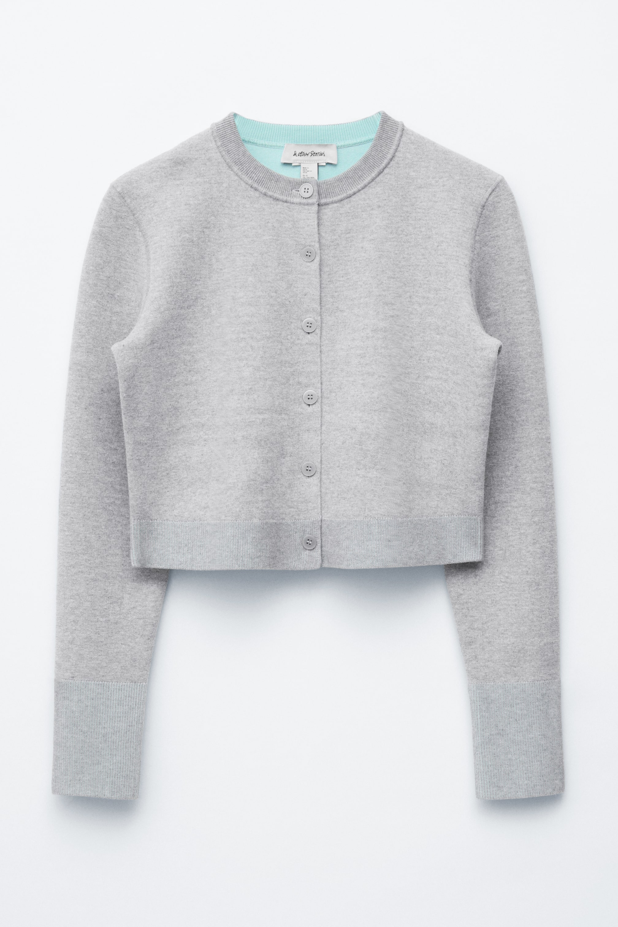 Grotere afbeelding bekijken: De VOORKANT van een lichtgrijs, kort vest toont een fijne breistructuur en lange mouwen. Het heeft een ronde halslijn met een contrasterende lichtblauw-groene binnenkant, een knoopsluiting aan de voorkant met tonale grijze knopen, en lichtgrijze geribbelde manchetten en zoom.