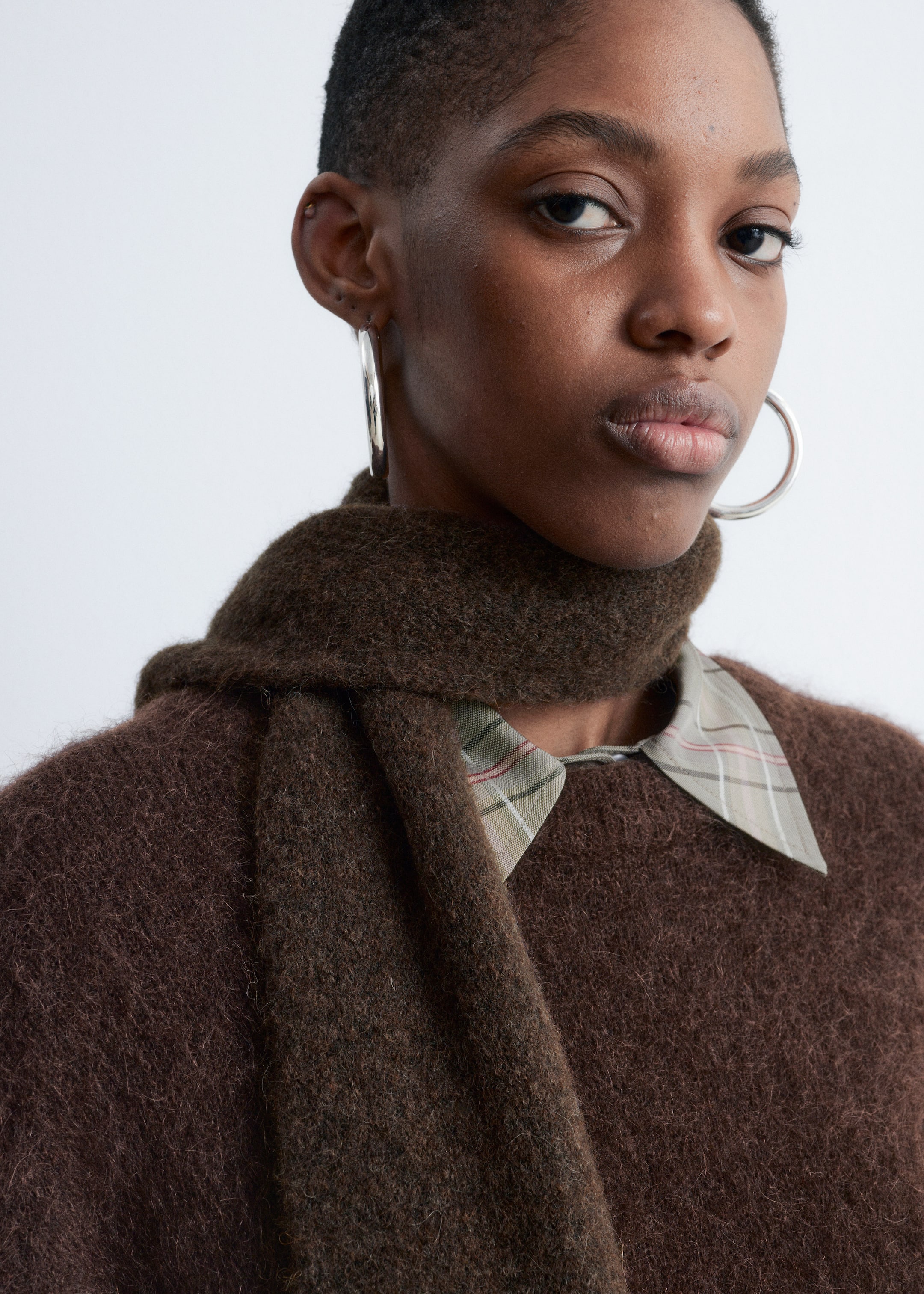 View larger image: A dark brown, fuzzy knit sweater is being worn, showing a textured surface. A light green plaid shirt collar is peeking out from the sweater's neckline, and a matching dark brown, textured scarf is draped around the neck over the sweater.