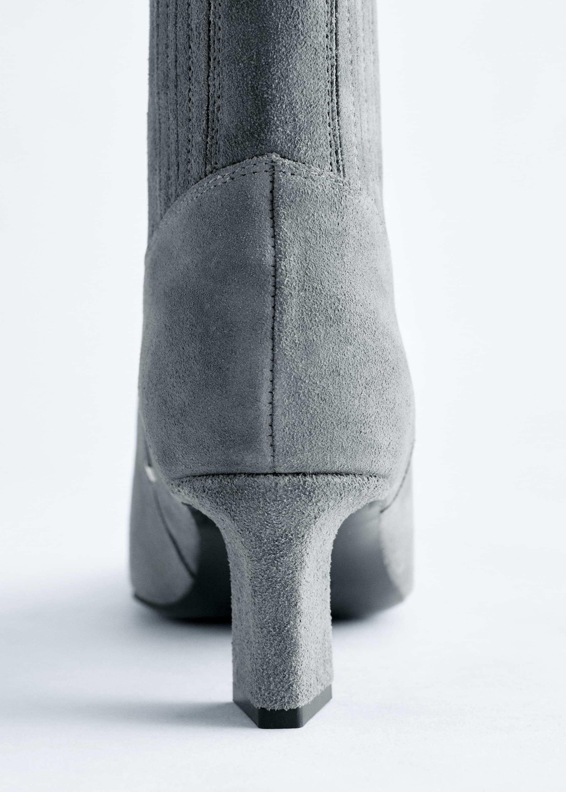 View larger image: A gray suede ankle boot is shown from the BACK, featuring a kitten heel and a prominent vertical seam running up the back of the shaft. Subtle elastic goring is visible on either side of the back seam.