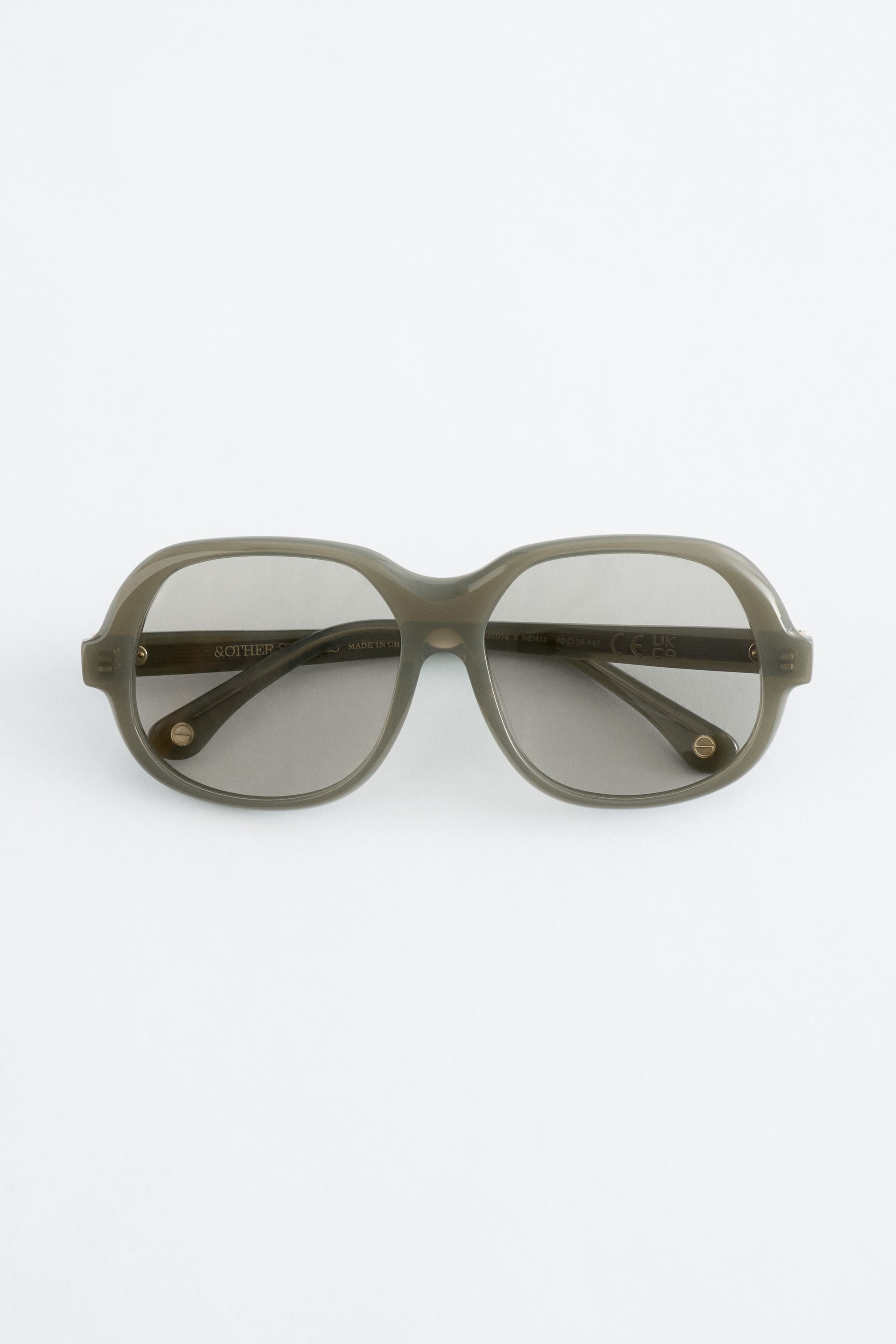 Agrandir l'image: Les lunettes de soleil présentent des montures épaisses et translucides de couleur vert olive avec des verres teintés foncés de forme rectangulaire arrondie, offrant une vue de face. De petits rivets circulaires de couleur dorée sont visibles sur les branches.
