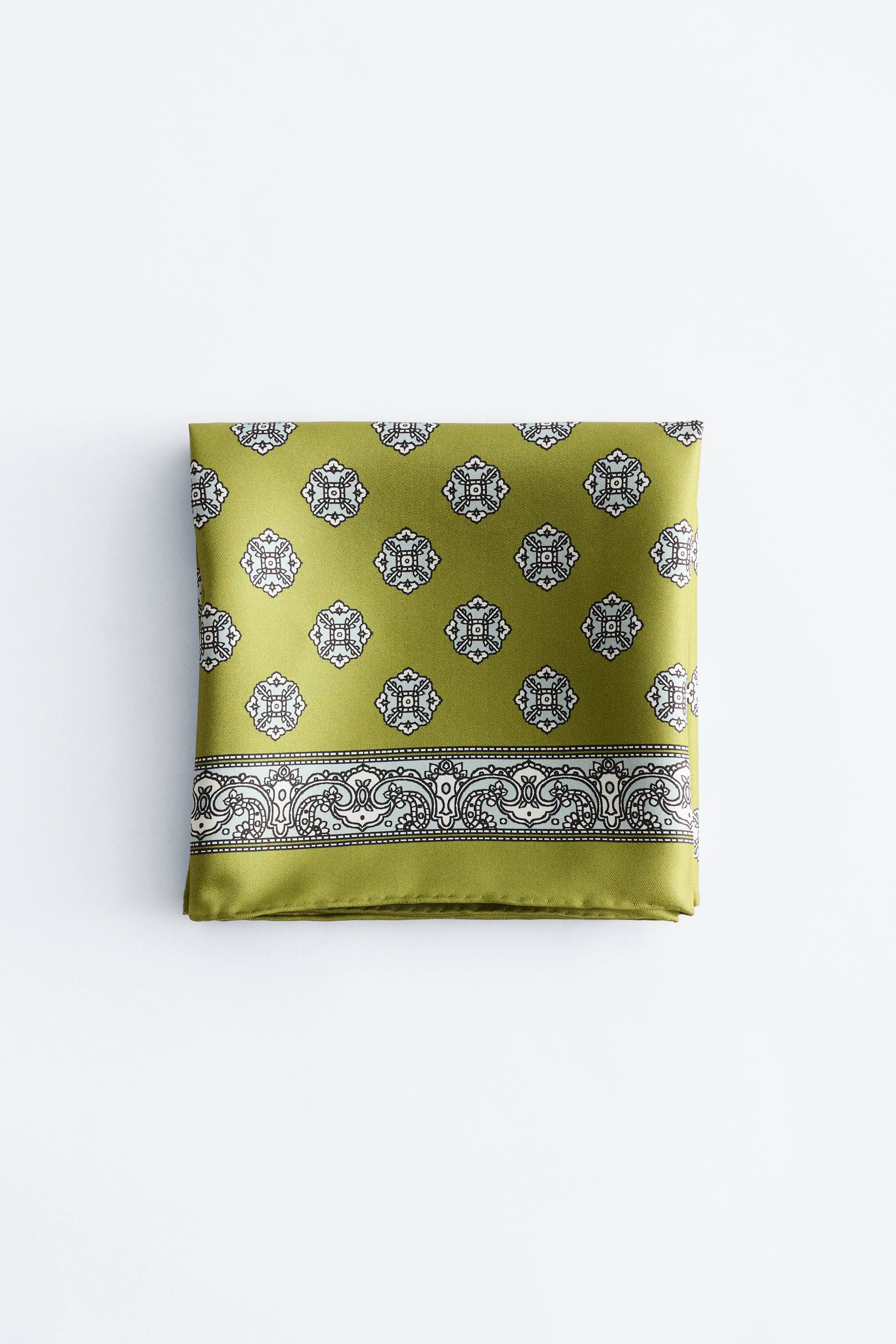 הצגת תמונה גדולה יותר: צעיף משי בצבע ירוק זית מקופל לריבוע, עם דוגמה גאומטרית בהירה החוזרת על עצמה על פני שטחו המרכזי ועיצוב שוליים מעוטר ומתפתל לאורך הקצה התחתון.