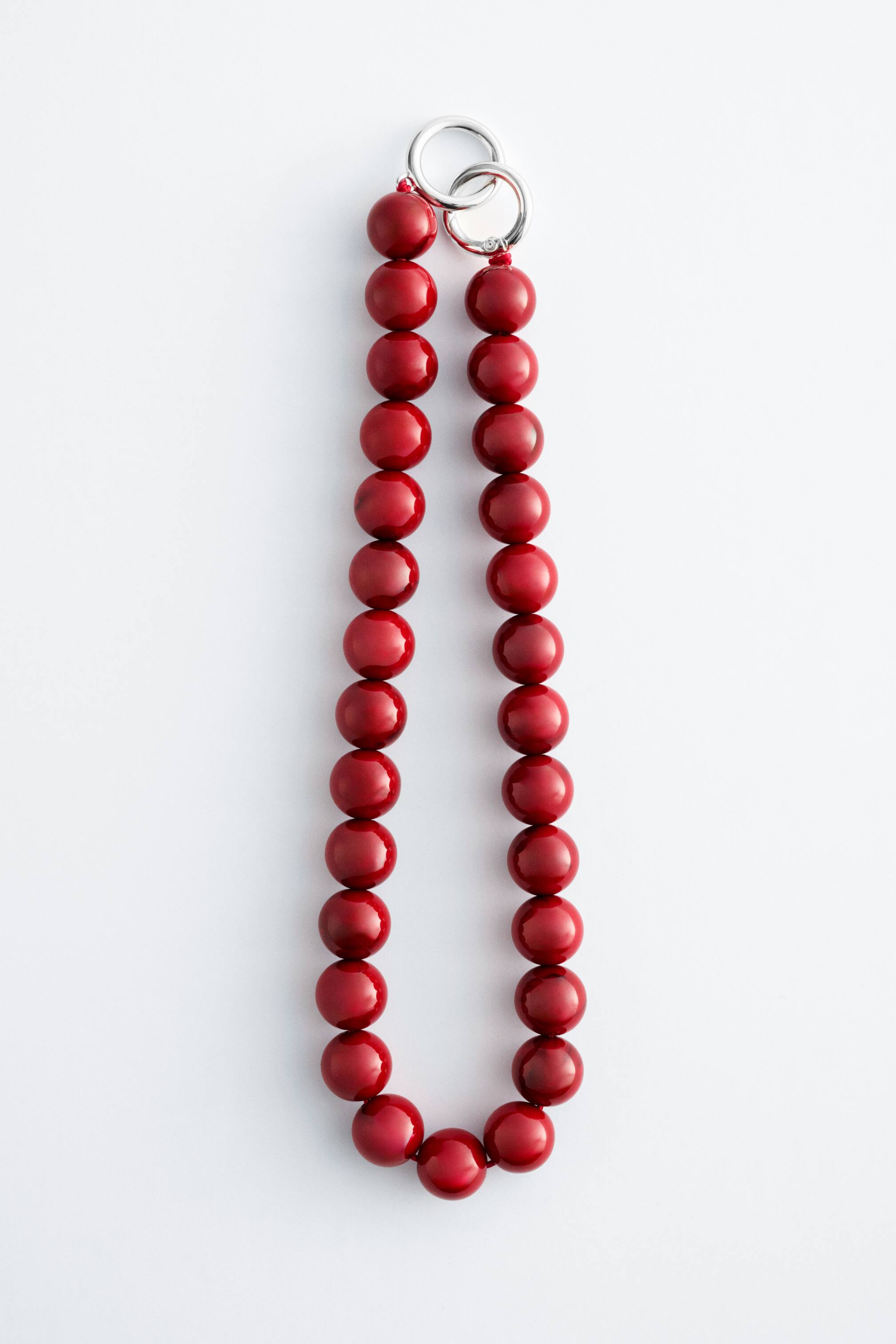 Agrandir l'image: Un collier court de perles en pierre présente des perles rouges brillantes et rondes, disposées en forme de U. Un fermoir délicat en forme d'anneau O de couleur argentée, avec deux anneaux entrelacés, est positionné en haut.