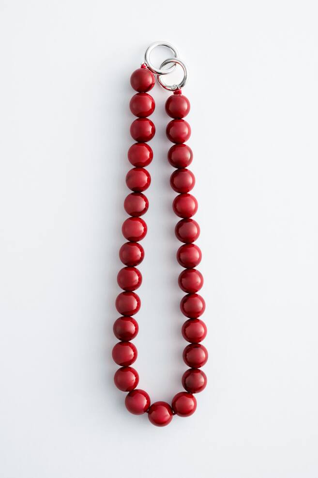 A short stone bead necklace featuring glossy, round red beads, arranged in a U-shape. A delicate silver-toned O-ring clasp, with two interlocked rings, is positioned at the top. - 1