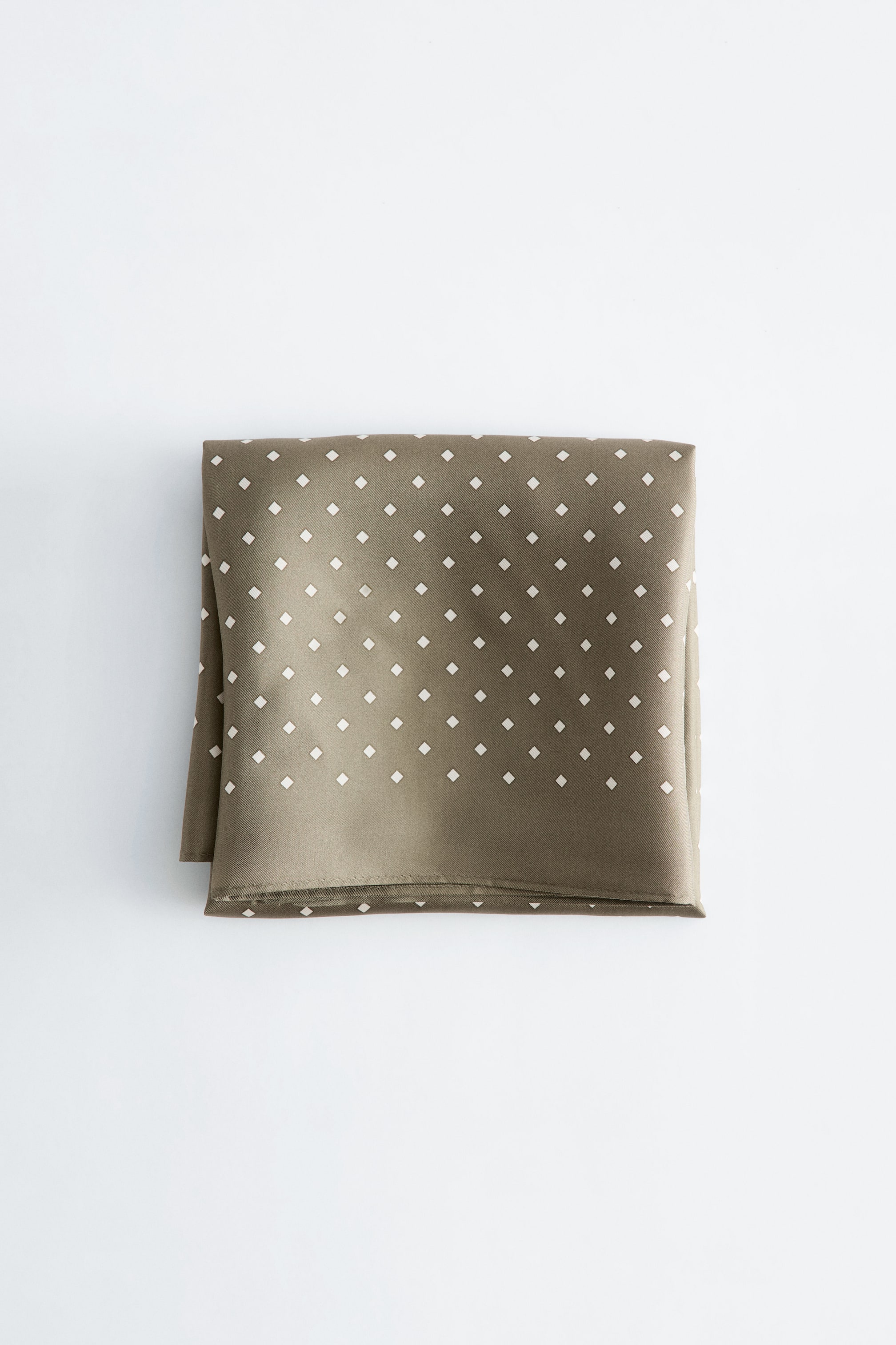 View larger image: An olive-green silk scarf, featuring a subtle diamond-dot print in white, is lying neatly folded.