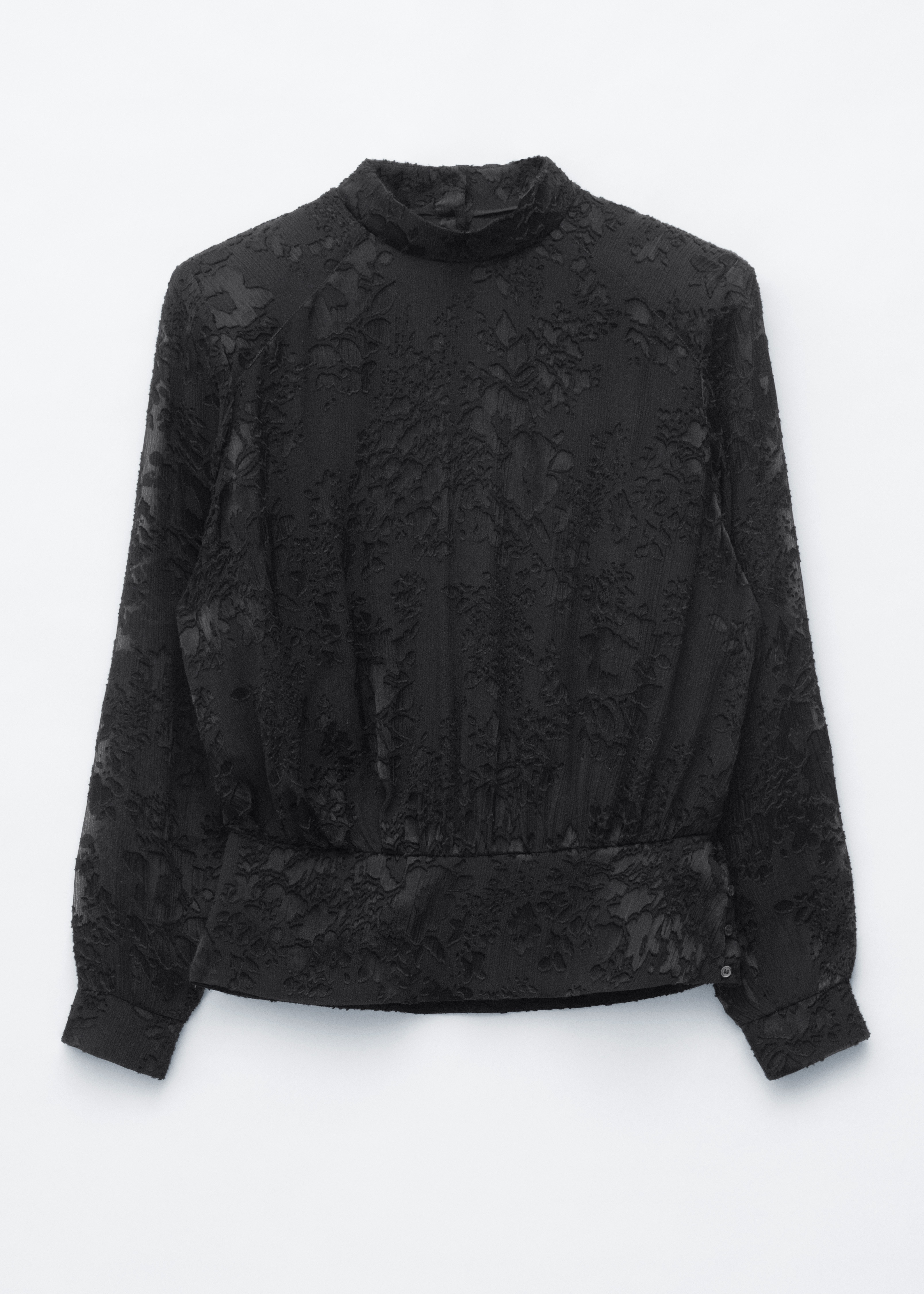 Eine schwarze Chiffonbluse mit floraler Textur, einem Stehkragen und strukturierten Schulterpolstern wird vom Model getragen. Die Bluse hat eine geraffte Taille und lange Ãrmel mit Bündchen und ist mit einer schwarzen Hose gestylt, während eine schwarze geflochtene Schultertasche über der Schulter getragen wird.