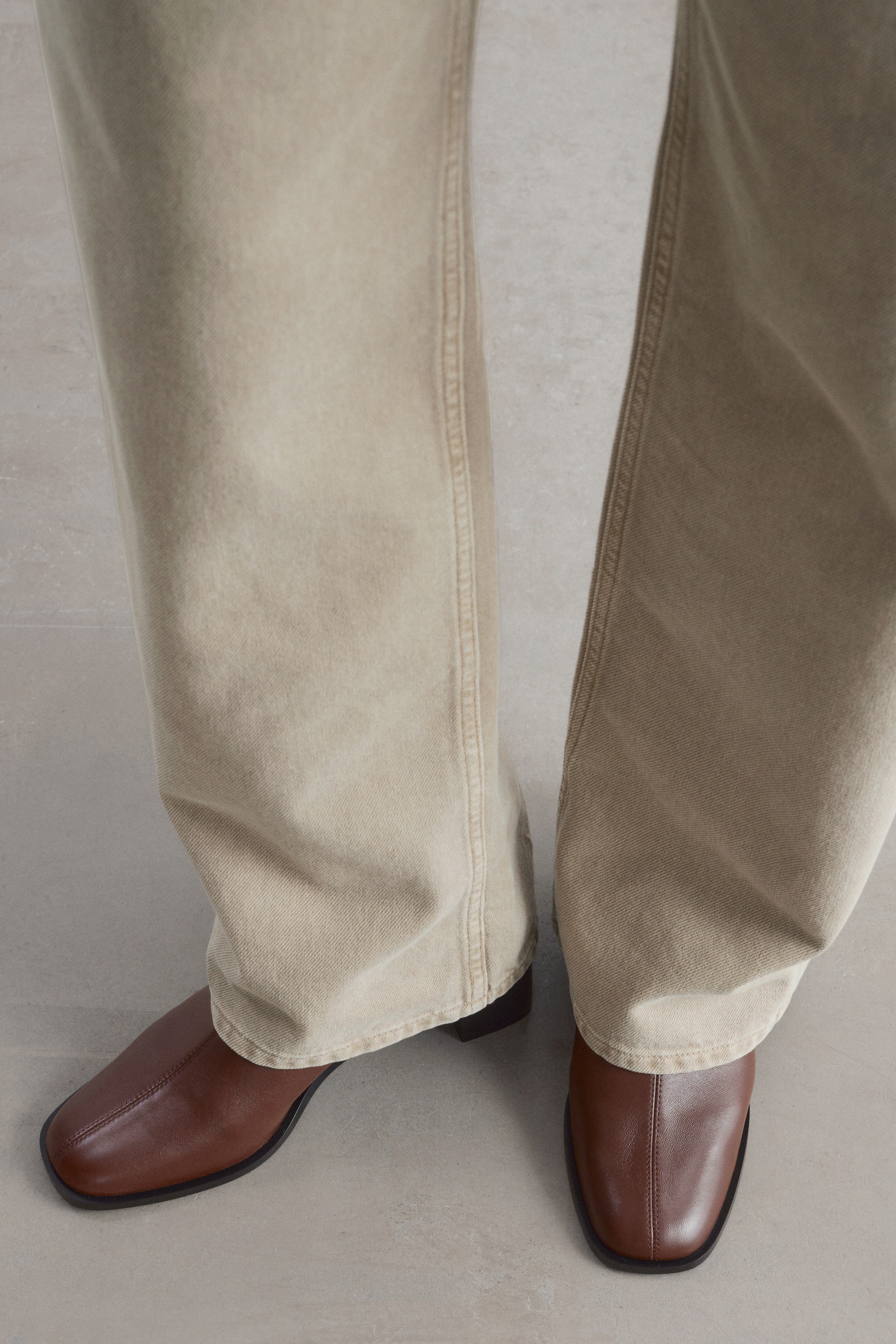 Agrandir l'image: Les bottines chaussettes Nappa en cuir marron sont vues de face, avec un bout carré et une couture centrale courant le long de l’empeigne. Un pantalon beige à jambe large retombe sur les chevilles, recouvrant partiellement les tiges des bottines.