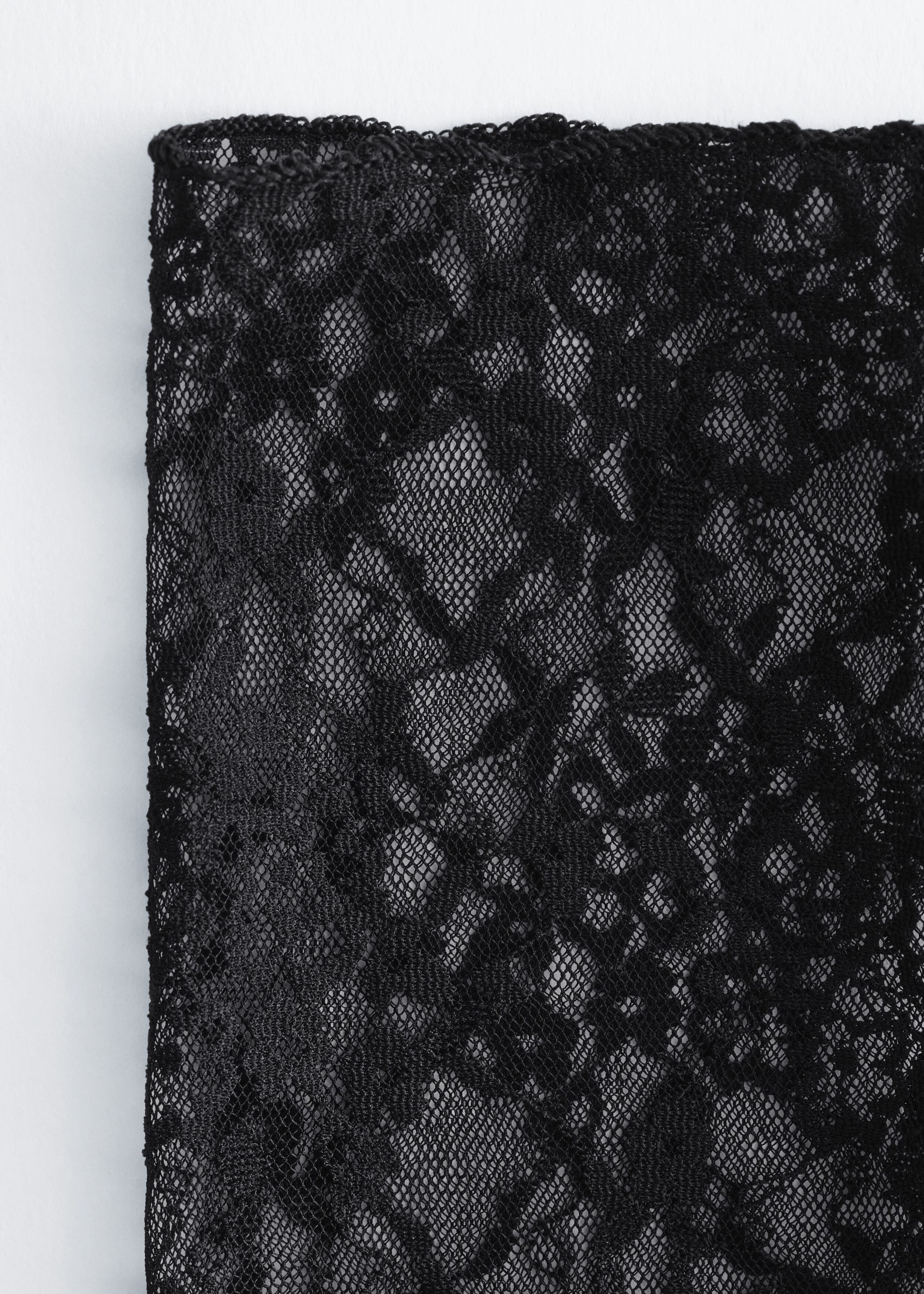 A black lace fingerless glove showcases an intricate floral pattern on sheer mesh fabric with a neat straight edge.