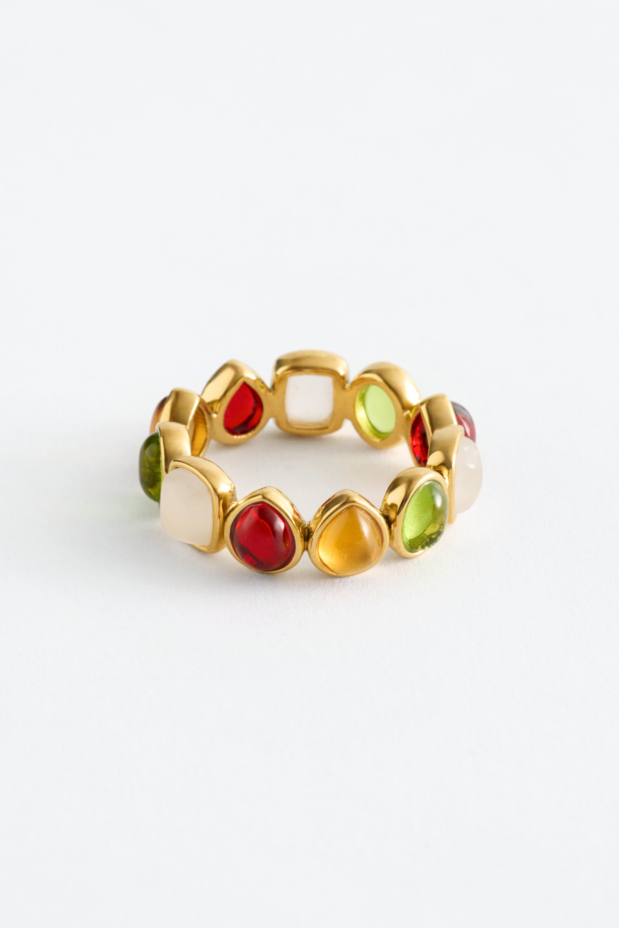 Größeres Bild anzeigen: Ein goldfarbener Ring präsentiert ein durchgehendes Band aus einzeln gefassten Steinen in unterschiedlichen Formen und Farben. Die Steine erscheinen in ovalen, quadratischen und tropfenartigen Formen und zeigen durchscheinende rote, gelbe und grüne Töne, neben opaken Cremefarben.