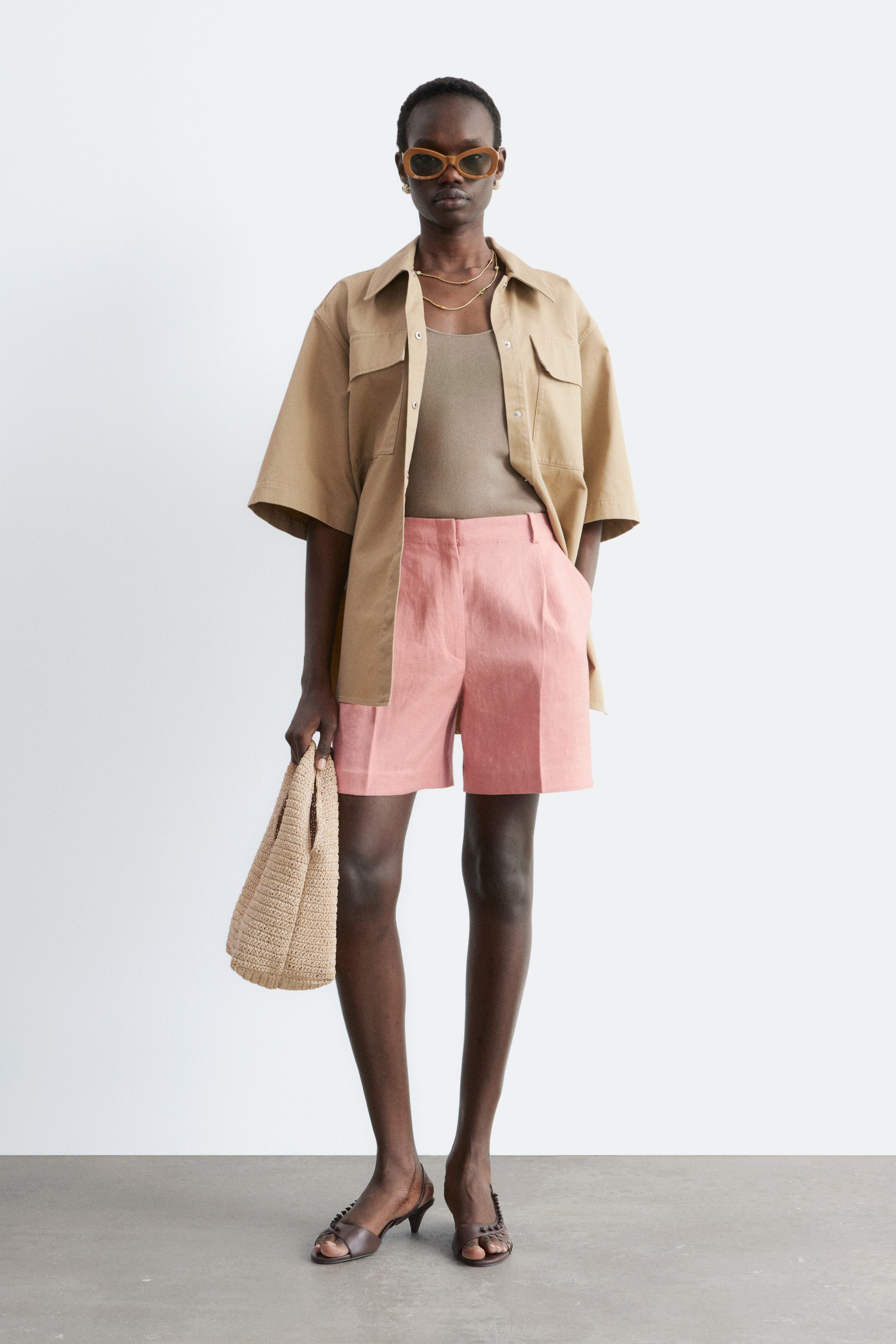 Grotere afbeelding bekijken: De roze linnen shorts worden gedragen door het model en reiken tot halverwege de dij. De shorts hebben voorplooien en schuine zijzakken, waarbij een van de handen van het model in een zak rust.