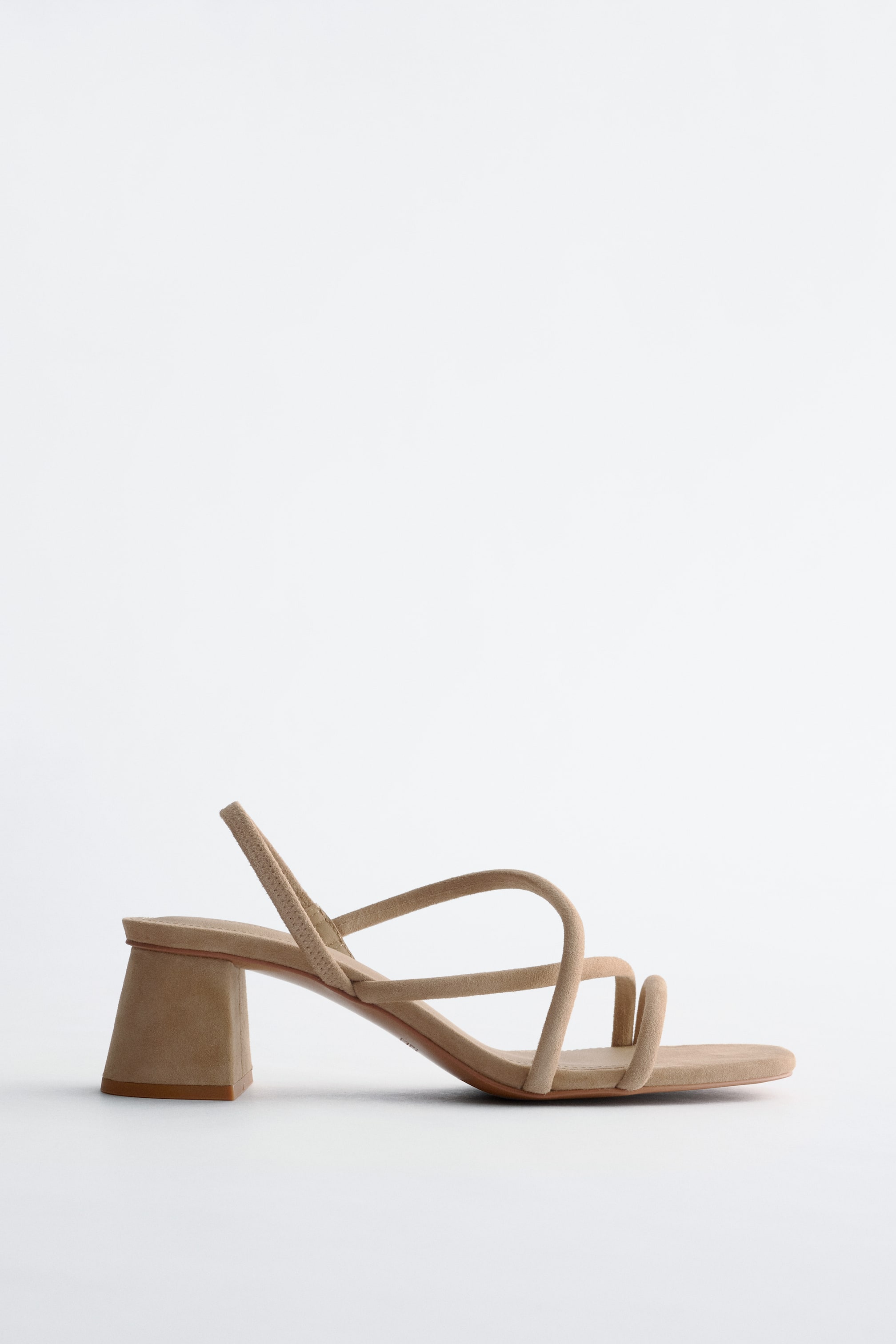 Vis større bilde: En beige sandal med blokkhel vises i sideprofil, laget av mykt skinn. Den har en minimalistisk stroppsilhuett med flere tynne stropper over foten, en firkantet tå, en blokkhel, og en elastisk bakstropp.
