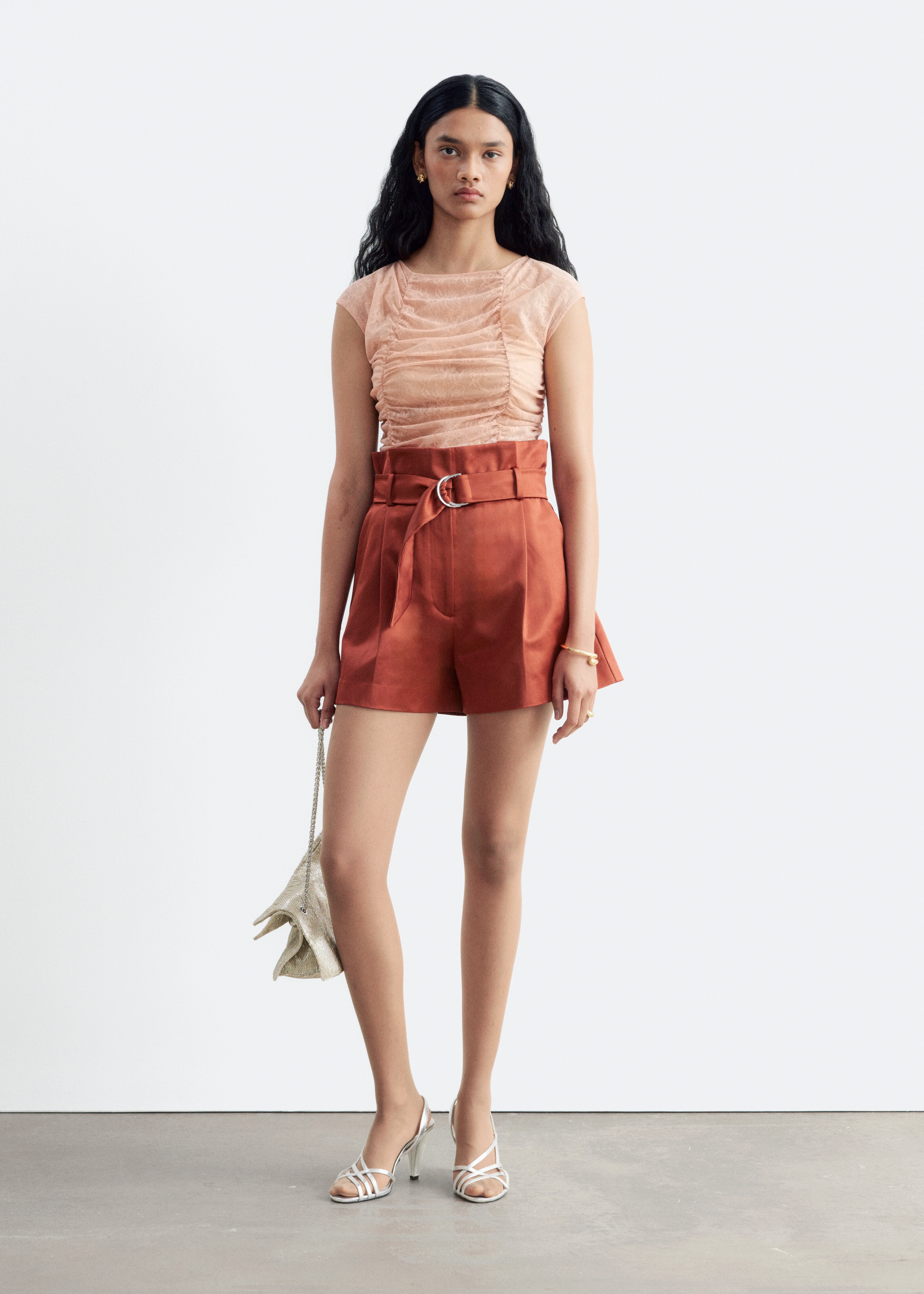 Une paire de shorts taille haute couleur rouille, dotÃ©s dâune taille paperbag avec une ceinture assortie en tissu et une boucle argentÃ©e Ã  double anneau en D, est prÃ©sentÃ©e de face. Les shorts affichent des pinces structurÃ©es sur le devant, des plis marquÃ©s au fer et des poches italiennes latÃ©rales inclinÃ©es.