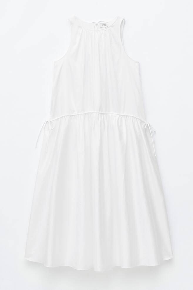 Ein weißes ärmelloses Kleid zeigt seine Vorderseite. Es verfügt über Raffungen am runden Ausschnitt und einen Tunnelzug mit Bindebändern an der Taille. Das Kleid fällt in einer lockeren Silhouette. - 1
