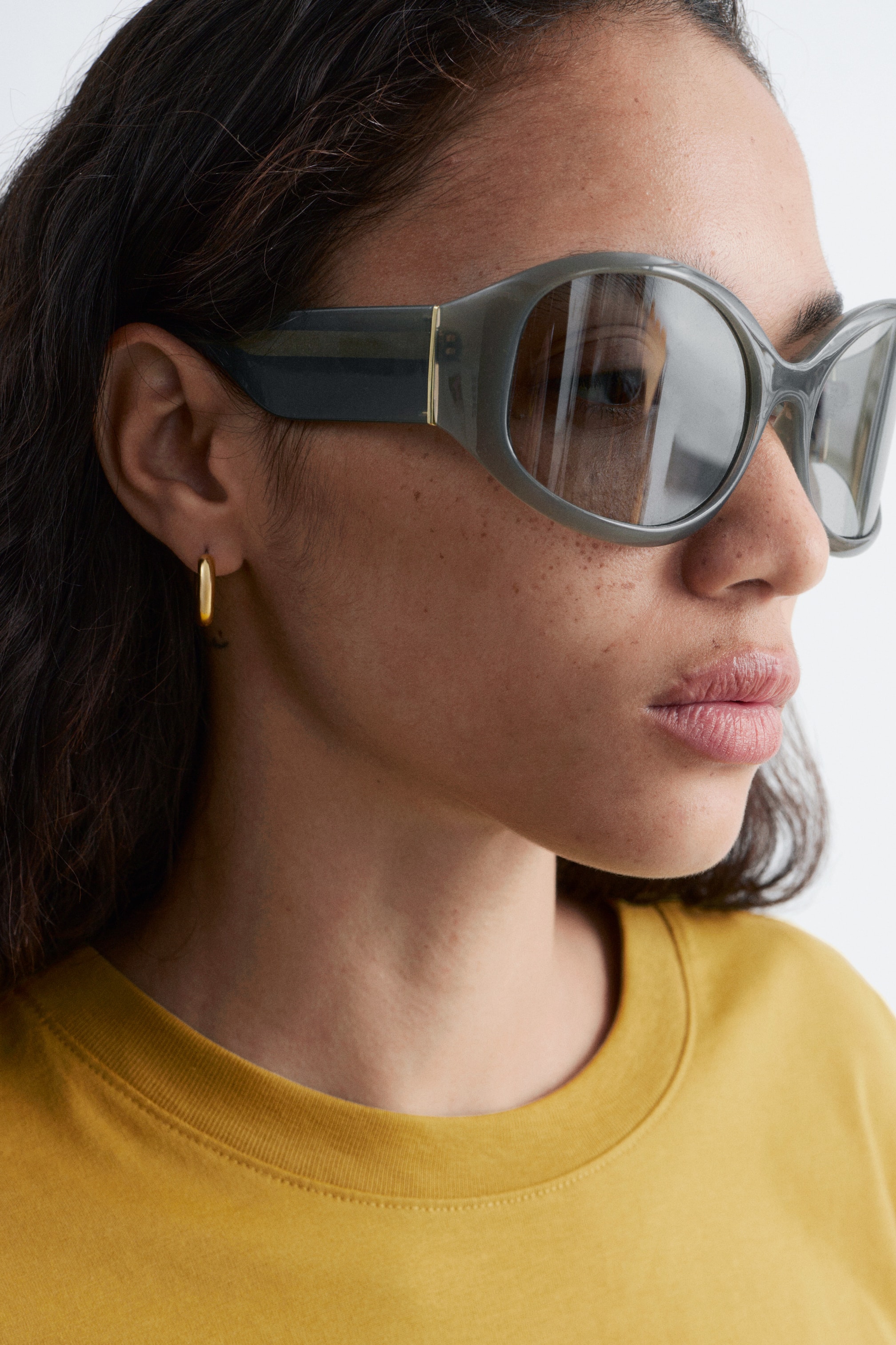 Grotere afbeelding bekijken: Oversized donkergrijze zonnebrillen worden van opzij getoond. Ze hebben dikke monturen, reflecterende lenzen en een subtiel goudkleurig accent op de pootjes.