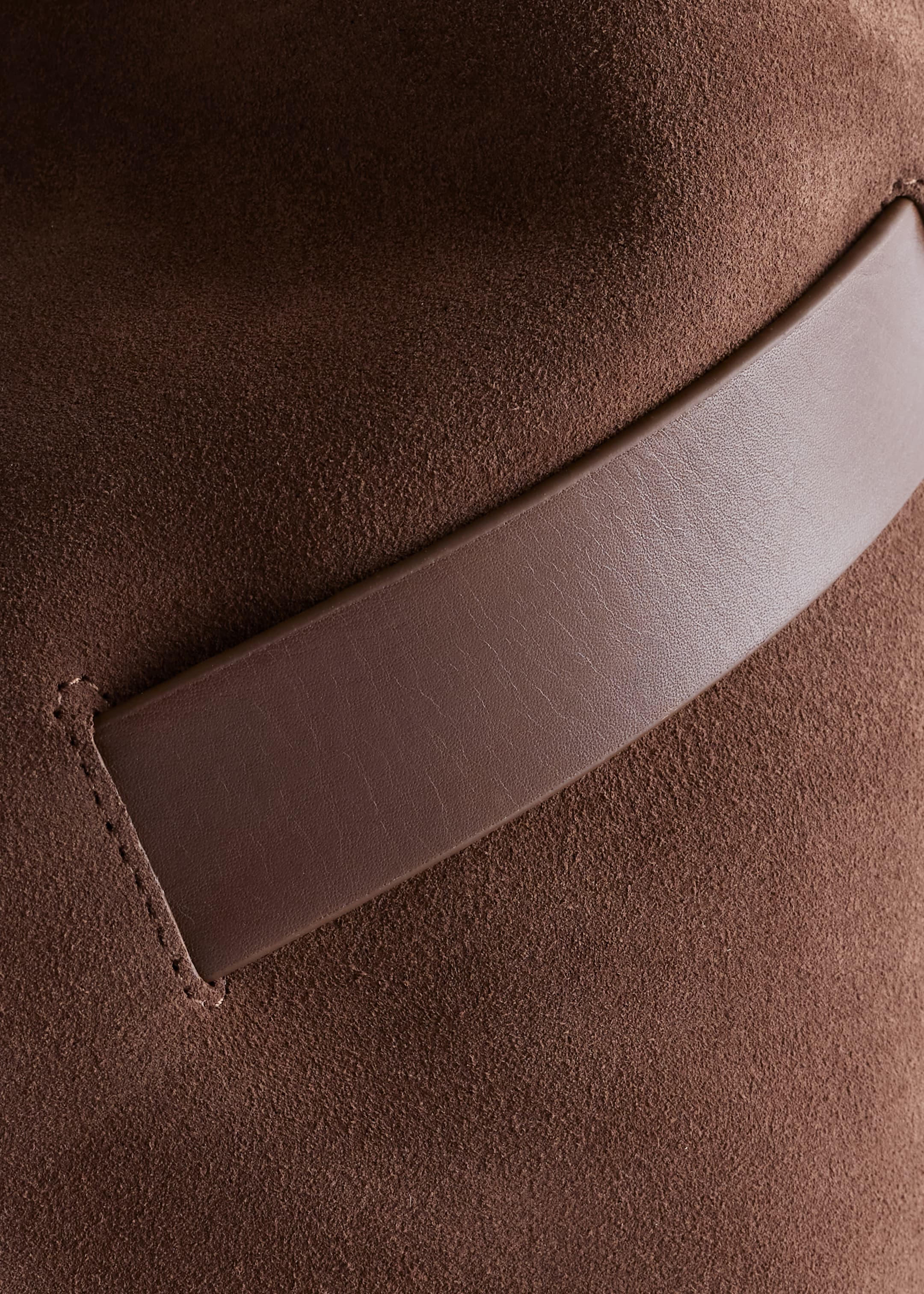 View larger image: A brown suede bucket bag is showing a close-up of its textured surface, with a contrasting smooth brown leather trim being sewn into the suede.