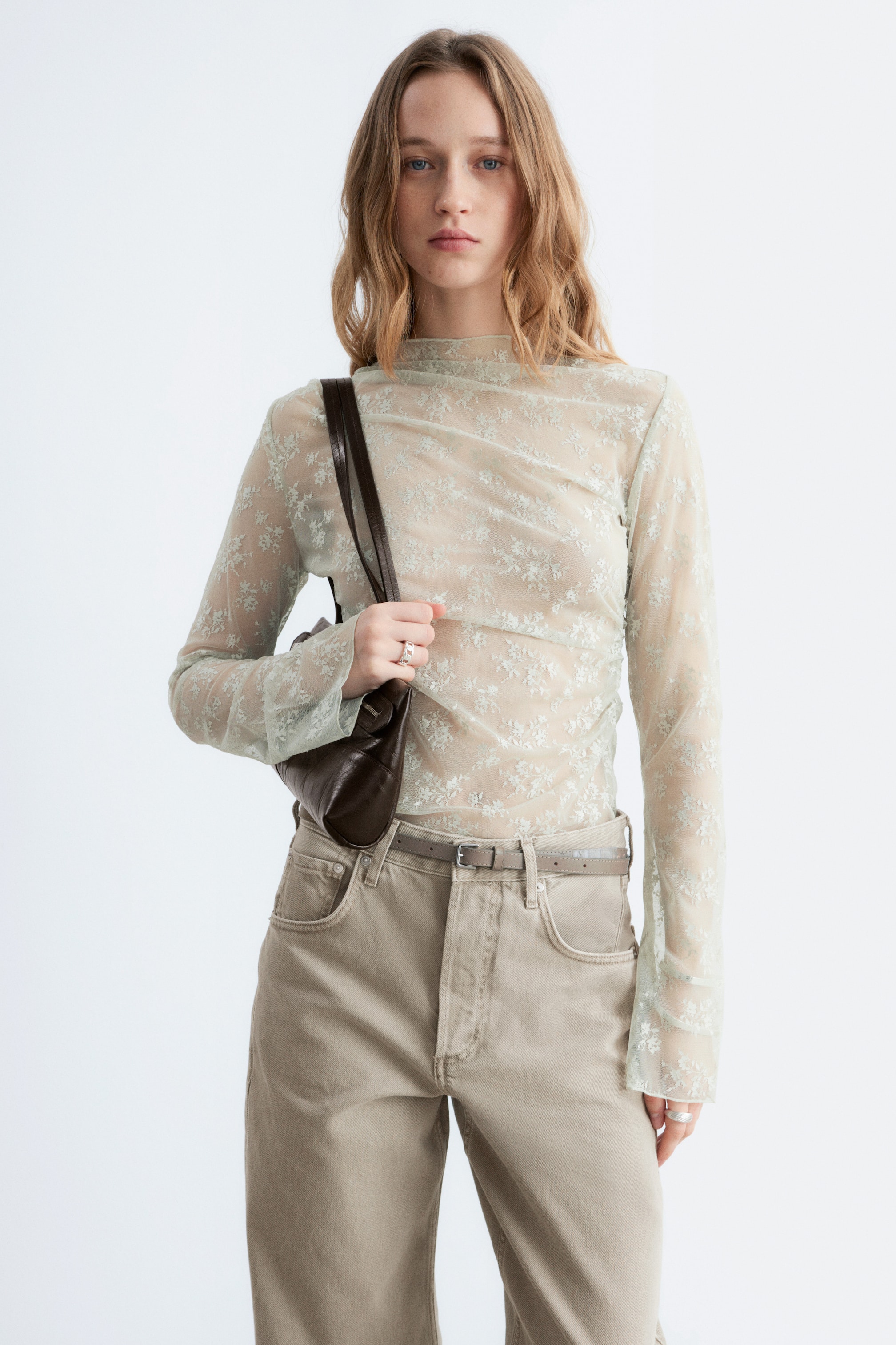 Ver imagem maior: A blusa transparente de mangas compridas está a ser apresentada de frente, com uma cor verde menta clara e um padrão rendado floral por toda a peça. Apresenta uma gola alta e mangas compridas, ajustando-se ao corpo.