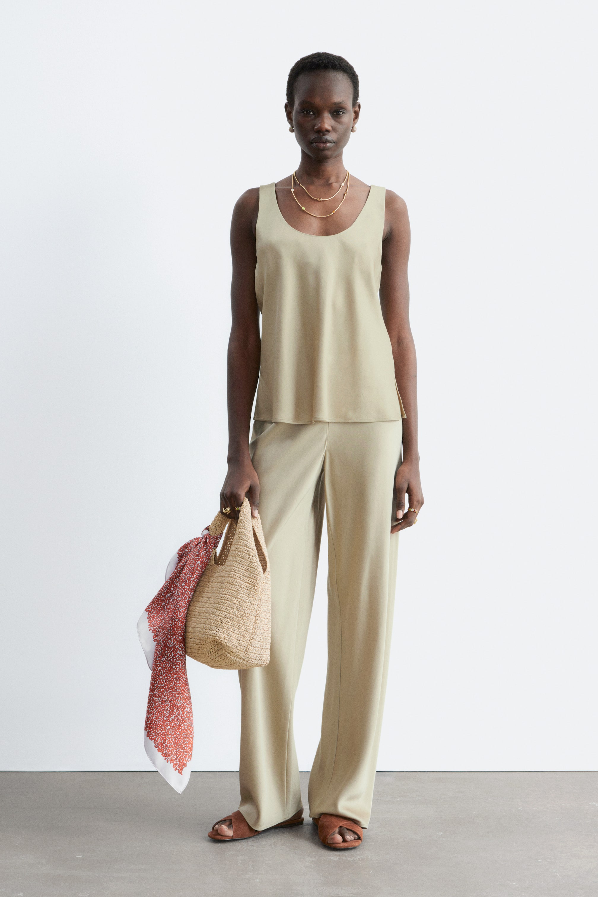Näytä suurempi kuva: Mallilla on yllään vaaleanbeige scoop-kaula-aukkoinen toppi, jossa on normaali istuvuus ja sivuhalkiot, yhdistettynä yhteensopiviin löysiin, leveälahkeisiin housuihin. Topissa on siisti kaula-aukko, ja housut esittelevät matalavyötäröisen siluetin ilman näkyviä sivusaumoja.
