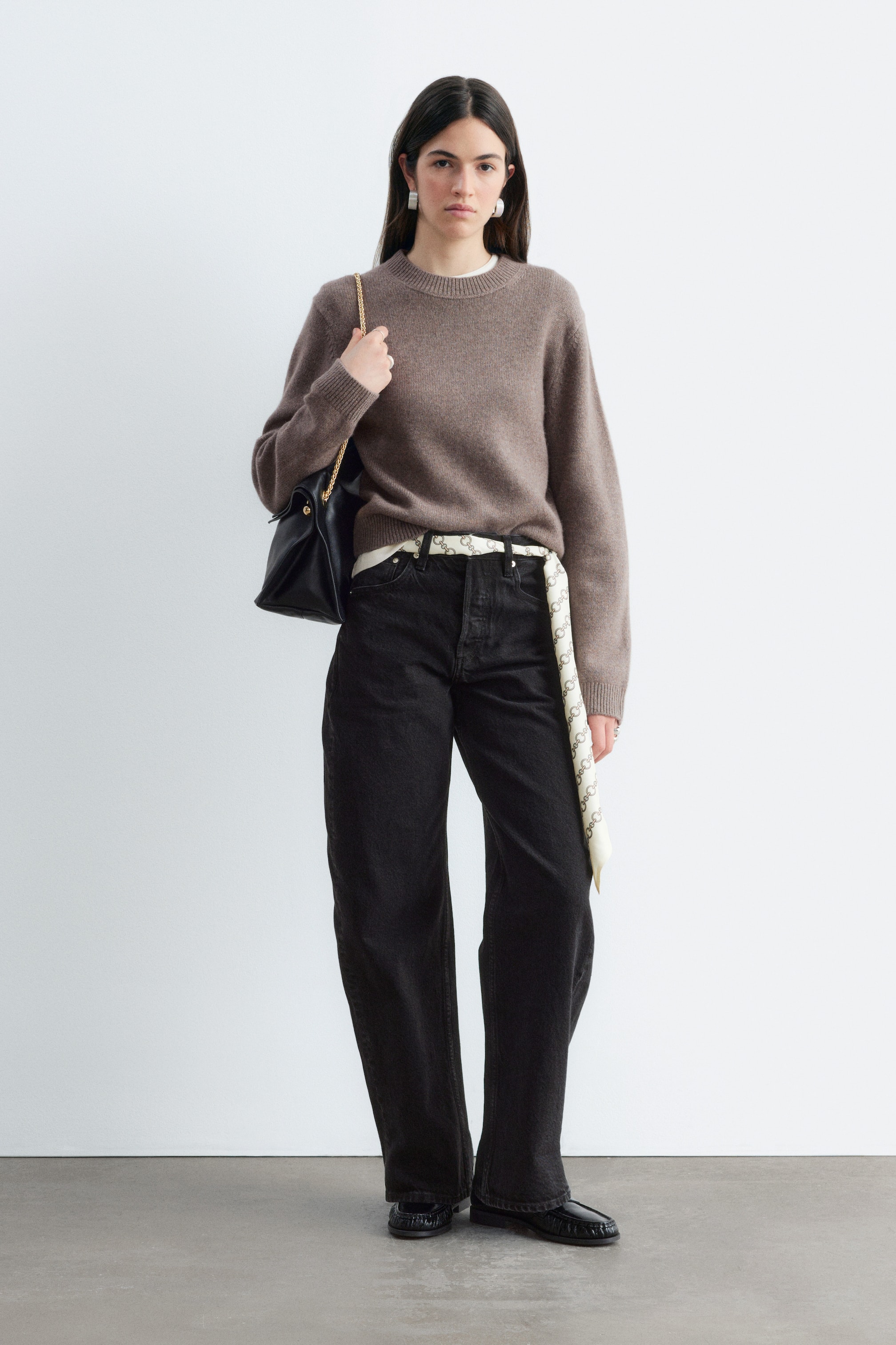 Größeres Bild anzeigen: Ein Pullover aus Kaschmirmischung in Taupebraun wird vom Model getragen und zeichnet sich durch einen gerippten Rundhalsausschnitt, Bündchen sowie eine lockere Passform aus. Der Pullover ist in eine schwarze Wide-Leg-Jeans gesteckt, dazu wird eine schwarze Leder-Umhängetasche über der Schulter getragen.