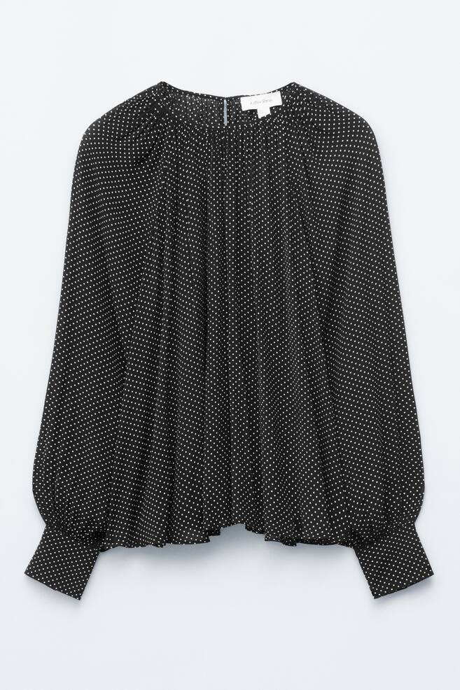 Eine schwarze Bluse, von vorne betrachtet, mit einem kleinen weißen Polka-Dot-Muster. Sie ist mit einem gerafften Rundhalsausschnitt, langen Puffärmeln und bandförmigen Manschetten gestaltet. - 1