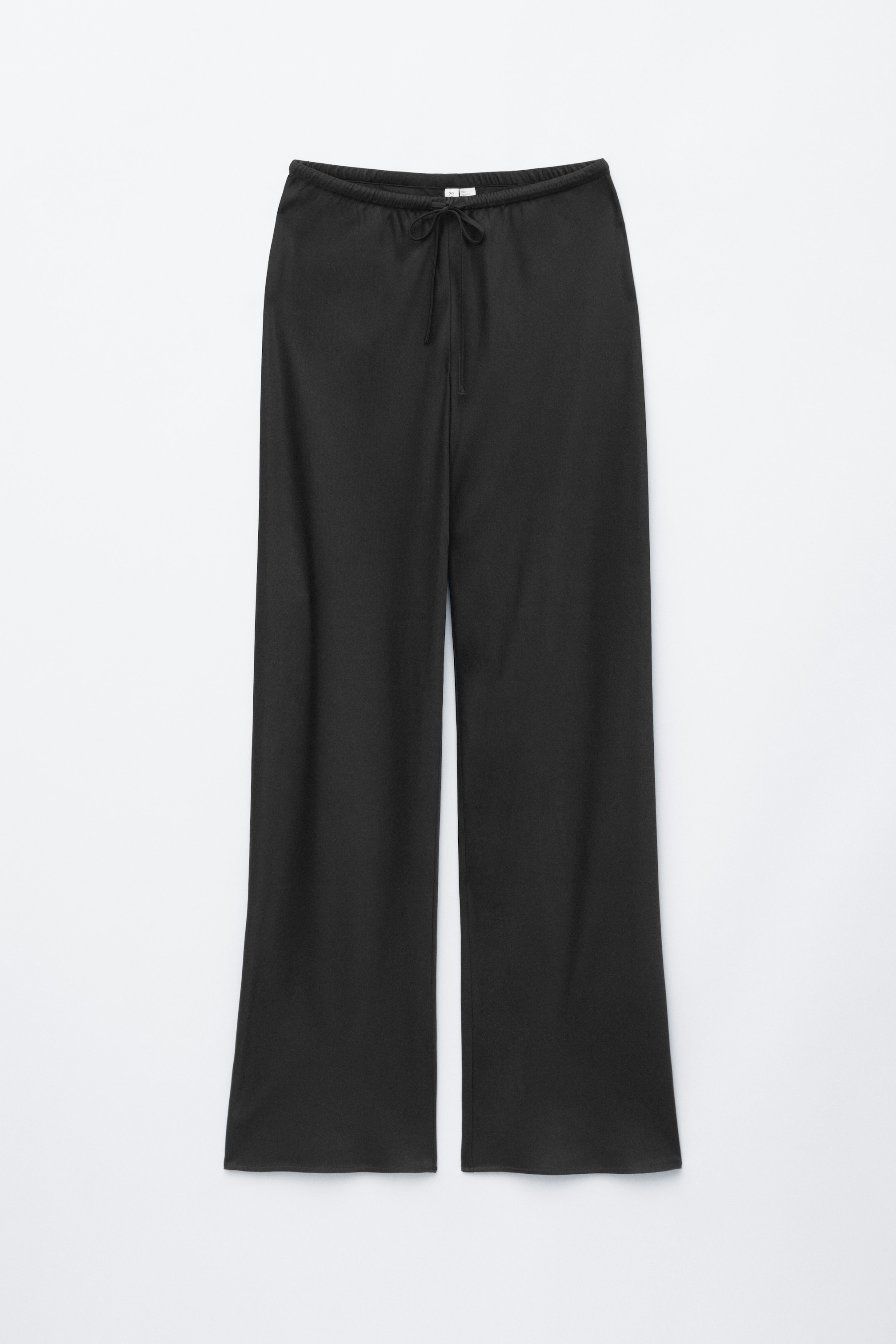 Agrandir l'image: Le pantalon noir est posé à plat, présentant une silhouette ample à jambes larges avec une taille élastiquée et un cordon de serrage noué à l'avant. Le tissu semble lisse, sans coutures latérales visibles.