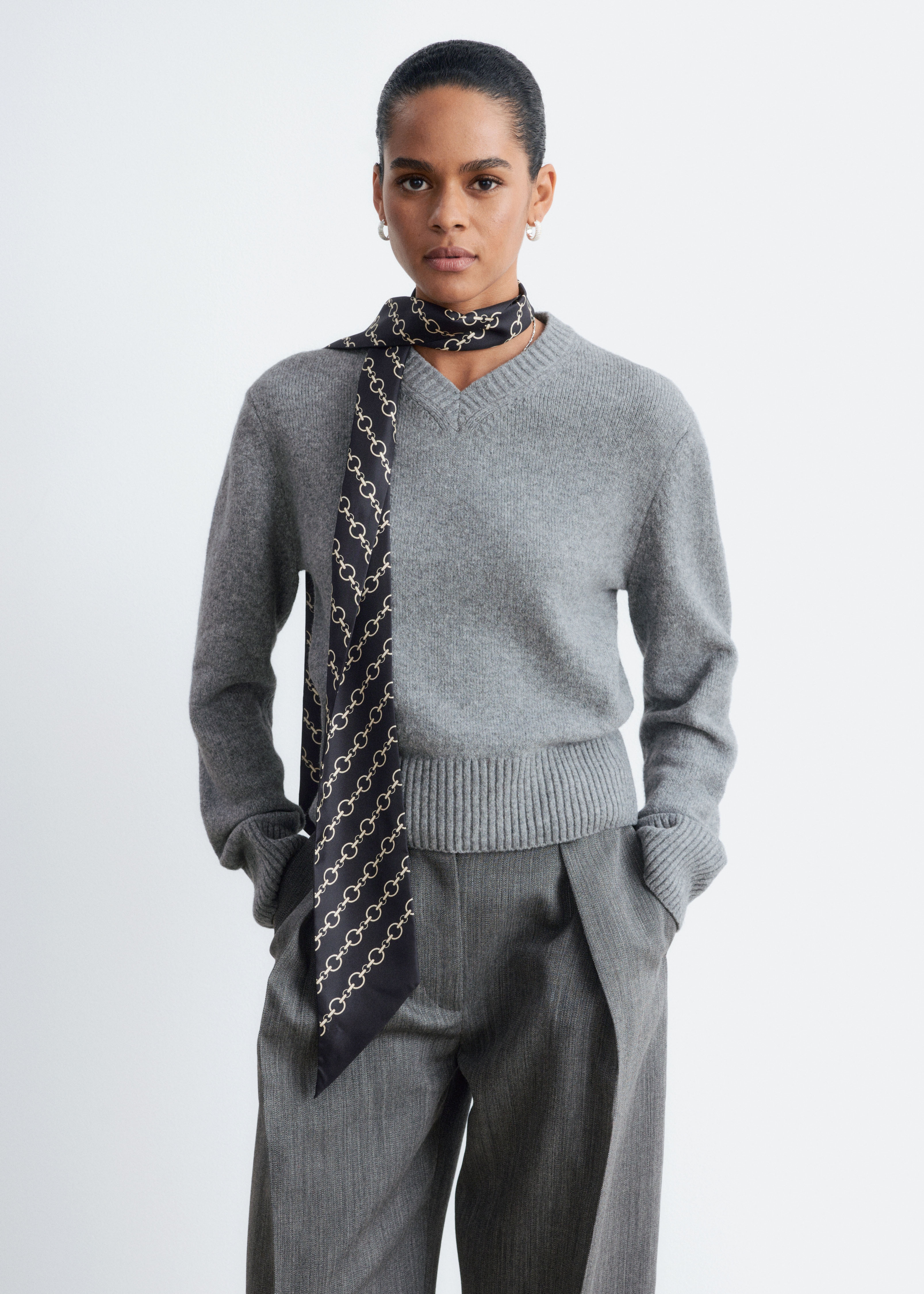 Ein grauer Strickpullover ist von vorne zu sehen und verfÃ¼gt Ã¼ber einen gerippten V-Ausschnitt, lange Ãrmel mit breiten RippbÃ¼ndchen und einen breiten gerippten Saum.
