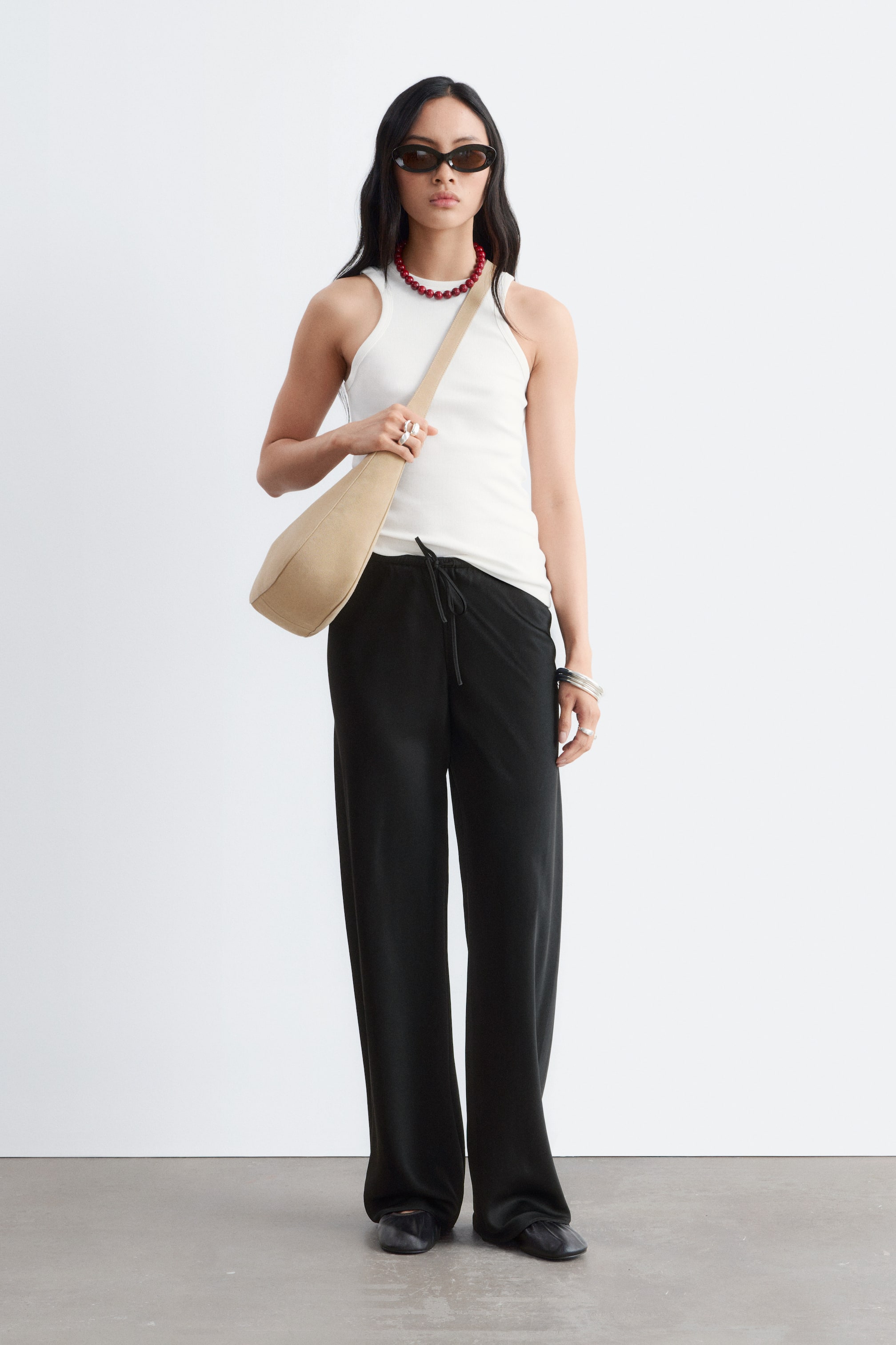 Visualizza l'immagine ingrandita: Pantaloni neri a gamba larga con vestibilità rilassata e un morbido tessuto a maglia drappeggiato con una sottile texture verticale, indossati frontalmente. Presentano una vita con coulisse e una lunghezza intera, con l'orlo che copre la parte superiore dei piedi.