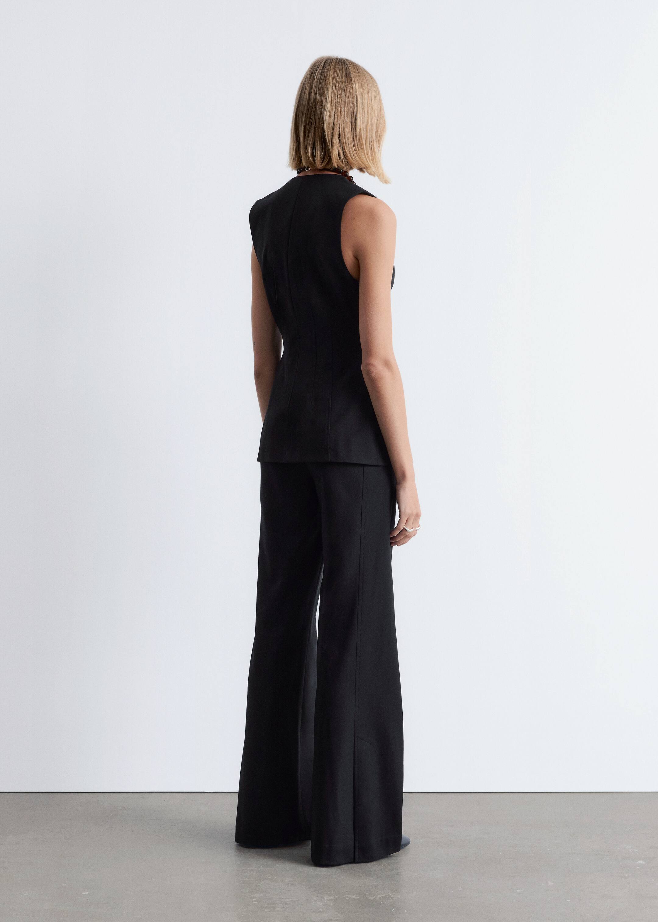 Agrandir l'image: Un haut noir sans manches et un pantalon noir à jambes larges sont présentés sur une silhouette, vue de dos et légèrement inclinée vers la droite. Le haut est ajusté à la taille et présente une couture verticale dans le dos, tandis que le pantalon a un pli marqué descendant le devant de chaque jambe.