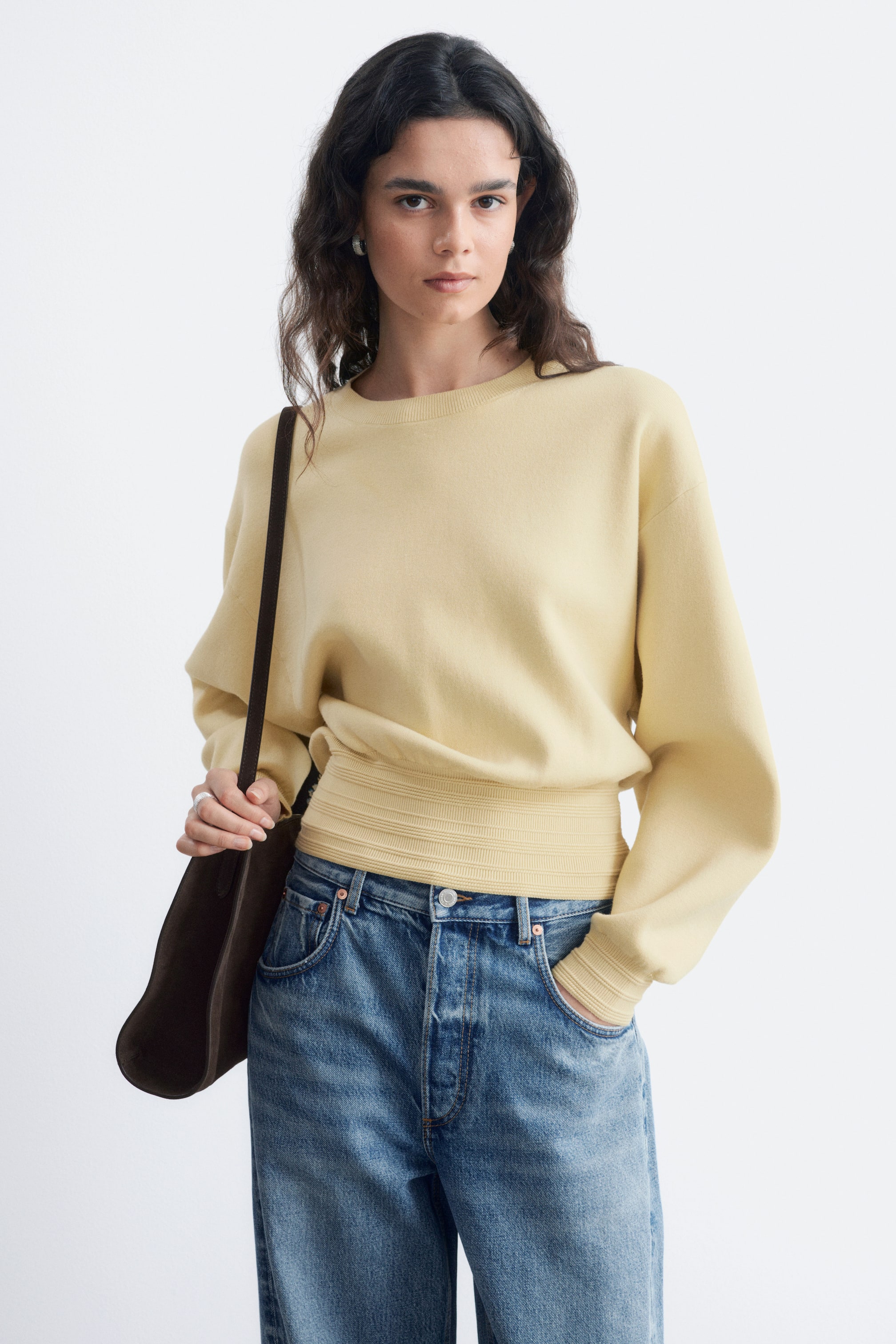 View larger image: A light yellow crew neck jumper features a loose-fitting body with long, voluminous sleeves and ribbed cuffs. A wide, horizontally ribbed waistband cinches the jumper at the waist.