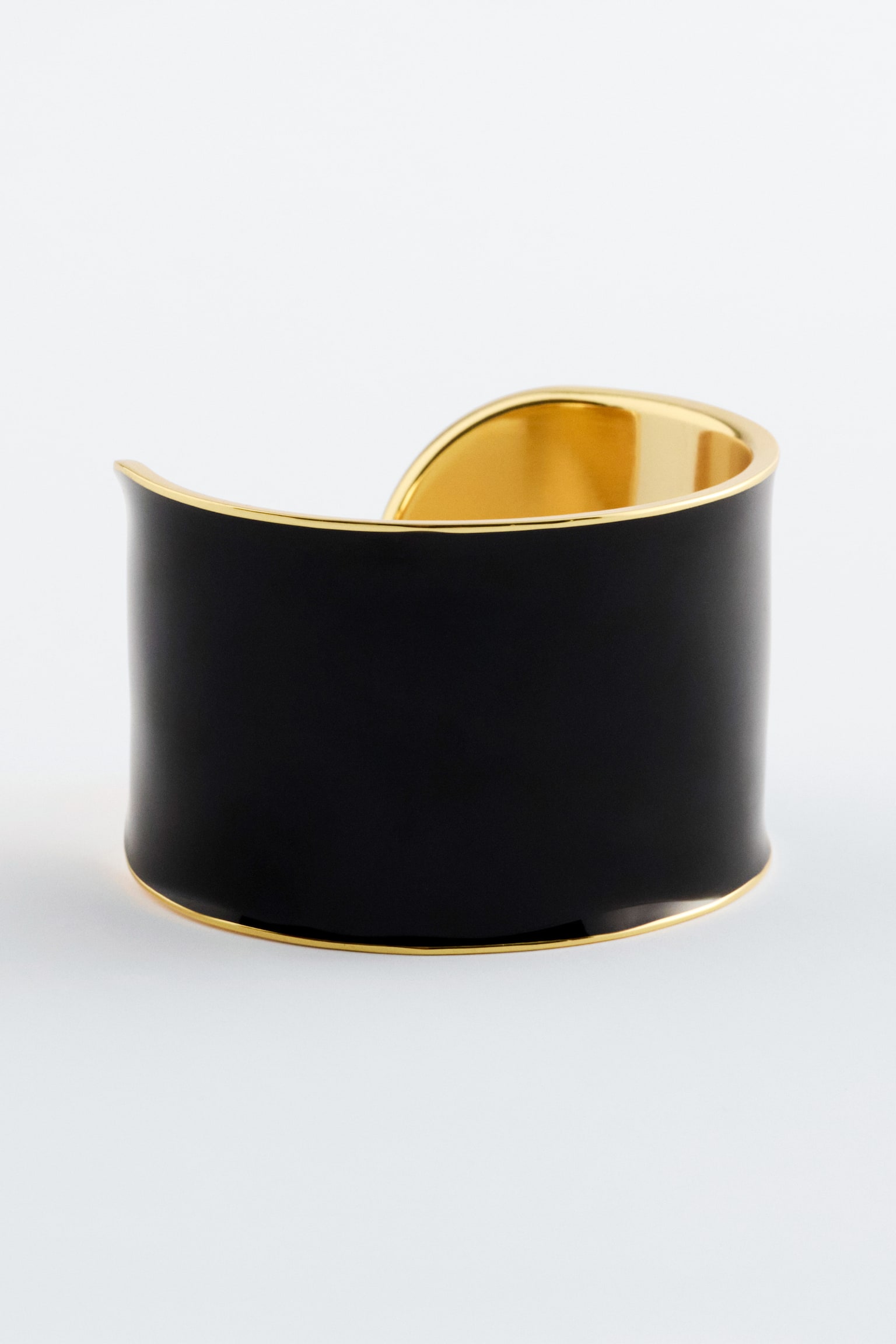 Un bracelet manchette en laiton poli est présenté de face, avec une large bande extérieure noire. Il affiche un intérieur doré poli et des bords dorés raffinés le long du haut et du bas, créant un effet bicolore. - 1