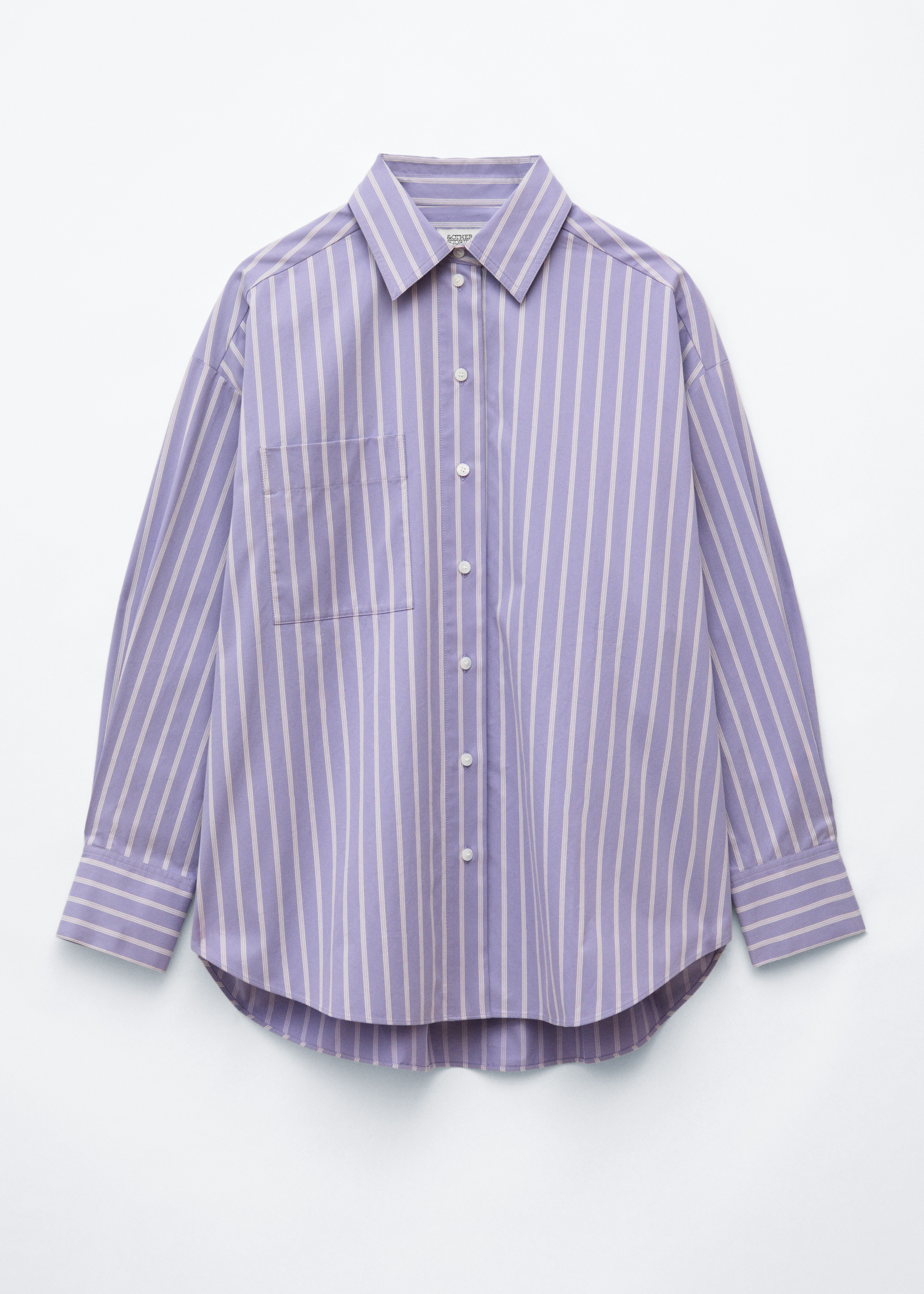 Mallilla on yllÃ¤Ã¤n oversized-tyylinen, vaaleanvioletti-valkoraidallinen pitkÃ¤hihainen paita, jossa on terÃ¤vÃ¤ kaulus, napitus edessÃ¤ ja rintatasku. Paita on stailattu mustan hameen kanssa, ja mallilla on musta punottu olkalaukku.