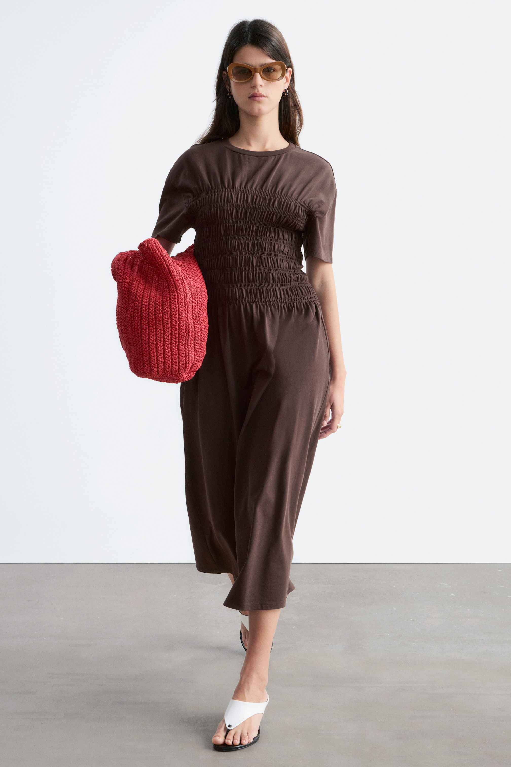 Προβολή μεγαλύτερης εικόνας: Ένα καφέ ολόσωμο ένδυμα με στρογγυλή λαιμόκοψη, κοντά μανίκια και σούρα στο μπούστο, που καταλήγει σε παντελόνι με φαρδιά μπατζάκια μέχρι τη μέση της γάμπας.