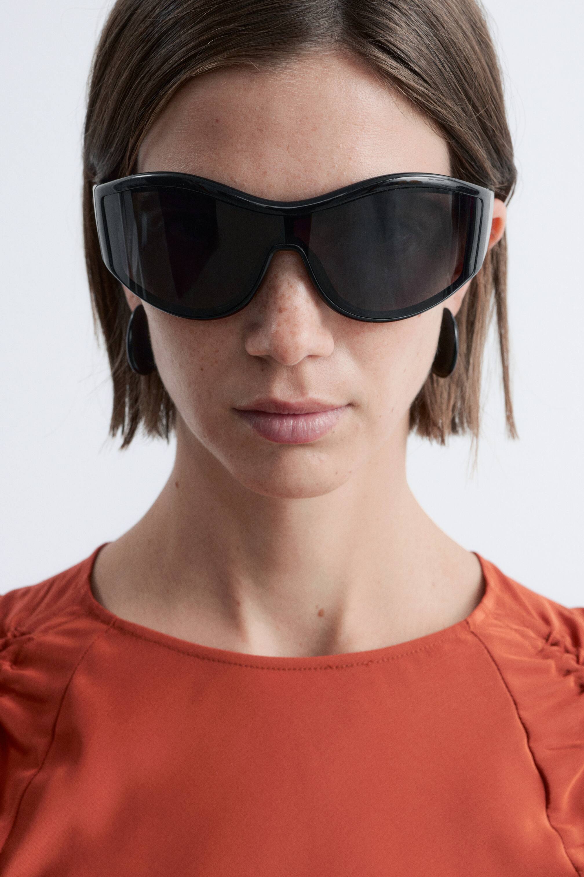 Ingrandisci l'immagine: Occhiali da sole neri oversize, con una montatura dolcemente arrotondata, lenti scure e aste larghe, indossati dalla modella.