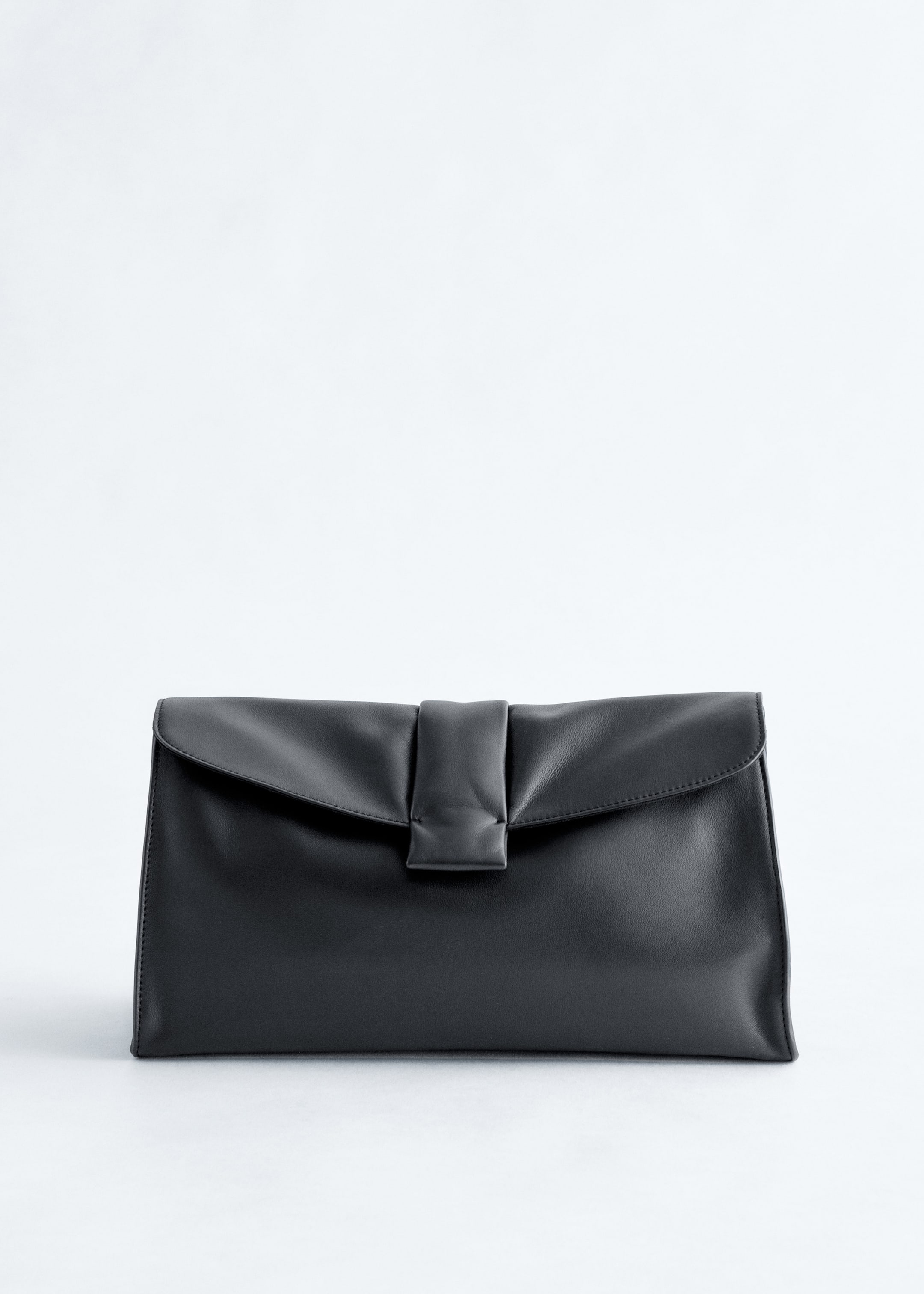 Größeres Bild ansehen: Eine schwarze, weiche Lederclutch wird von vorne gezeigt, mit einer Klappenverschluss, der mit einem zentralen vertikalen Riegel akzentuiert ist.