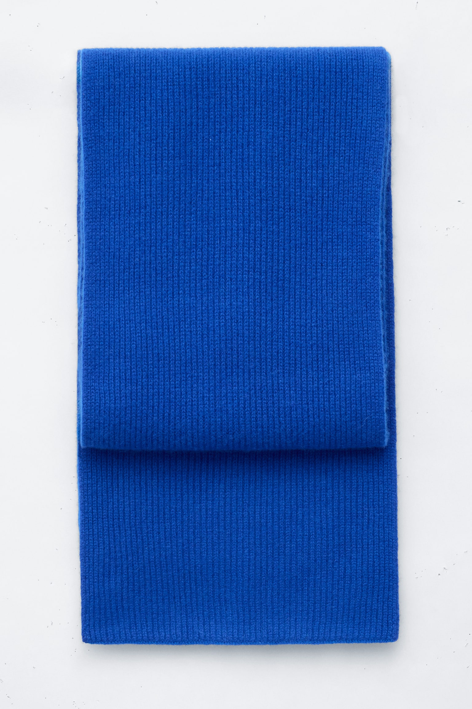 Una sciarpa in maglia di cashmere blu brillante Ã¨ posata piegata e distesa frontalmente, mostrando la sua fine texture a costine verticali e i bordi rettangolari puliti.