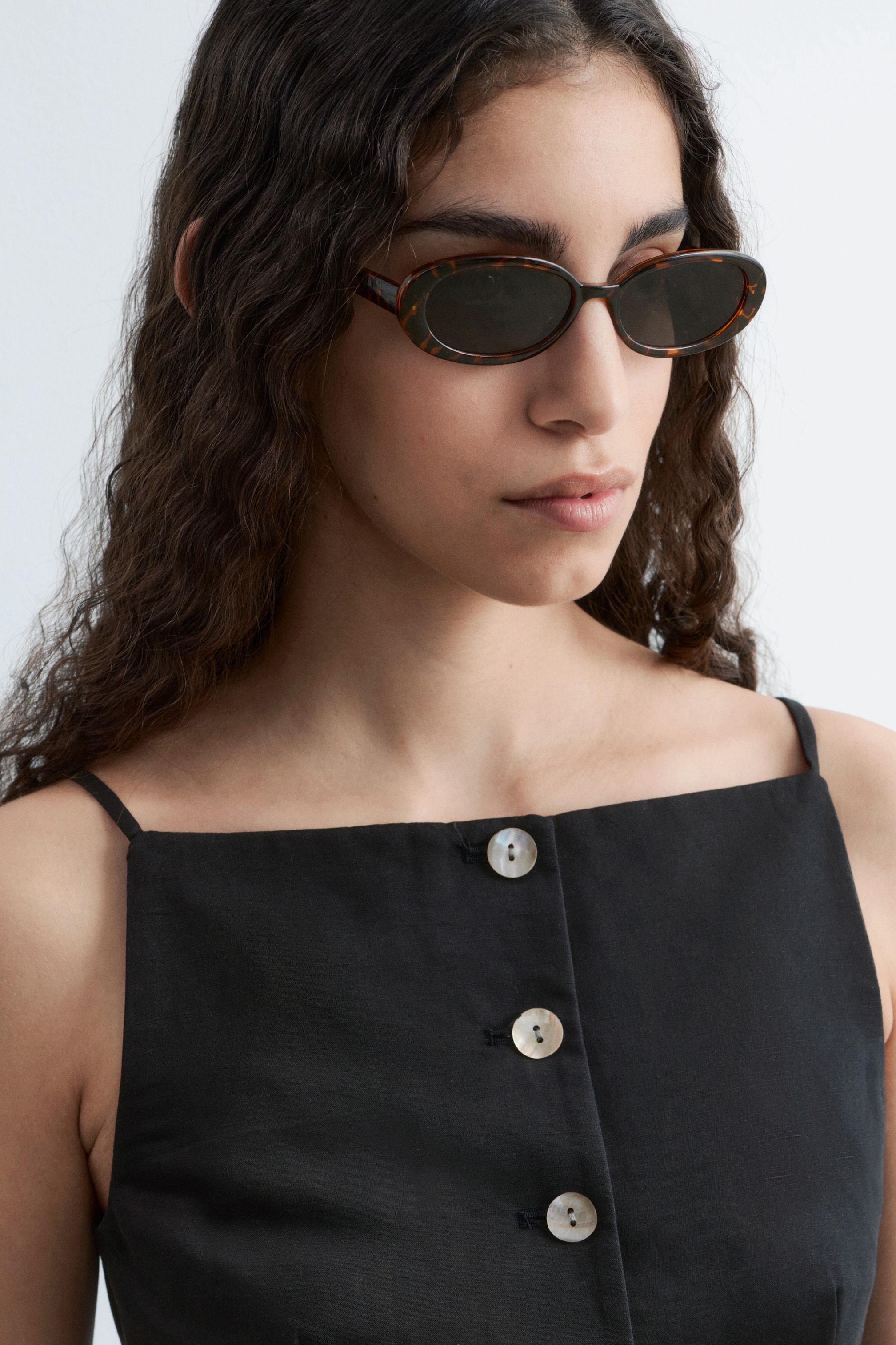 Agrandir l'image: Un haut noir à encolure carrée doté de fines bretelles spaghetti. Trois boutons ronds iridescents sont visibles sur une patte de boutonnage légèrement inclinée à l'avant.