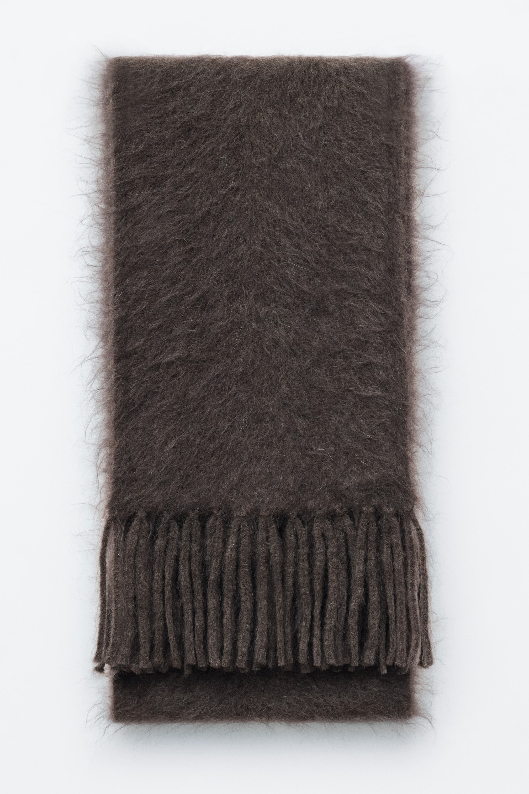 Visualizza immagine più grande: Una sciarpa in misto mohair e lana di colore marrone scuro è posata in piano in una vista frontale, mettendo in risalto una texture soffice e spazzolata con morbide fibre effetto alone lungo i bordi. La sciarpa, ripiegata con cura, mostra spesse frange attorcigliate sul bordo inferiore.