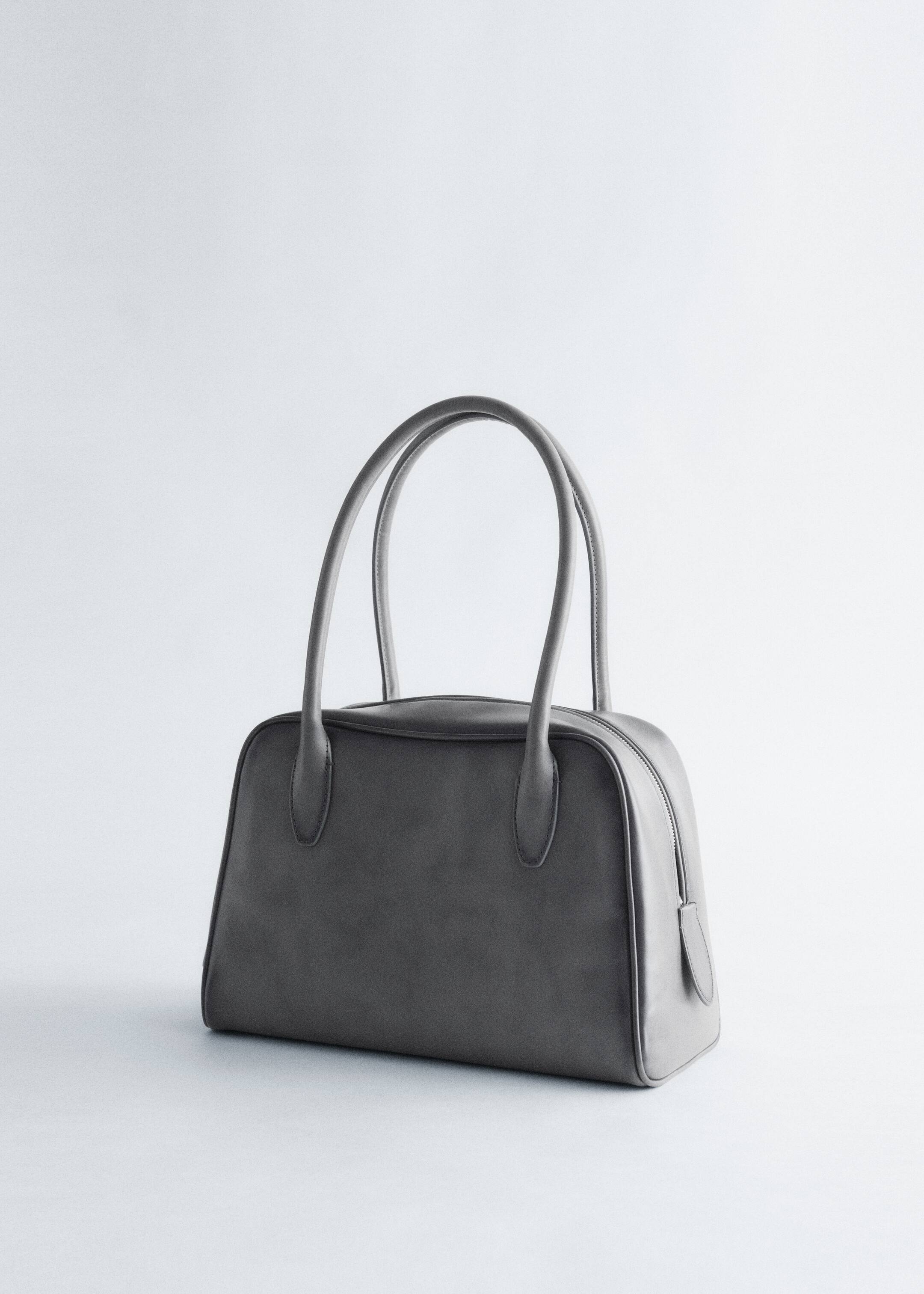 Grösseres Bild ansehen: Eine strukturierte, dunkelgraue Handtasche präsentiert sich mit einer rechteckigen Basis und abgerundeten oberen Kanten. Sie verfügt über zwei hohe, abgerundete Tragegriffe und einen sichtbaren Reissverschluss, der entlang der Oberseite verläuft.