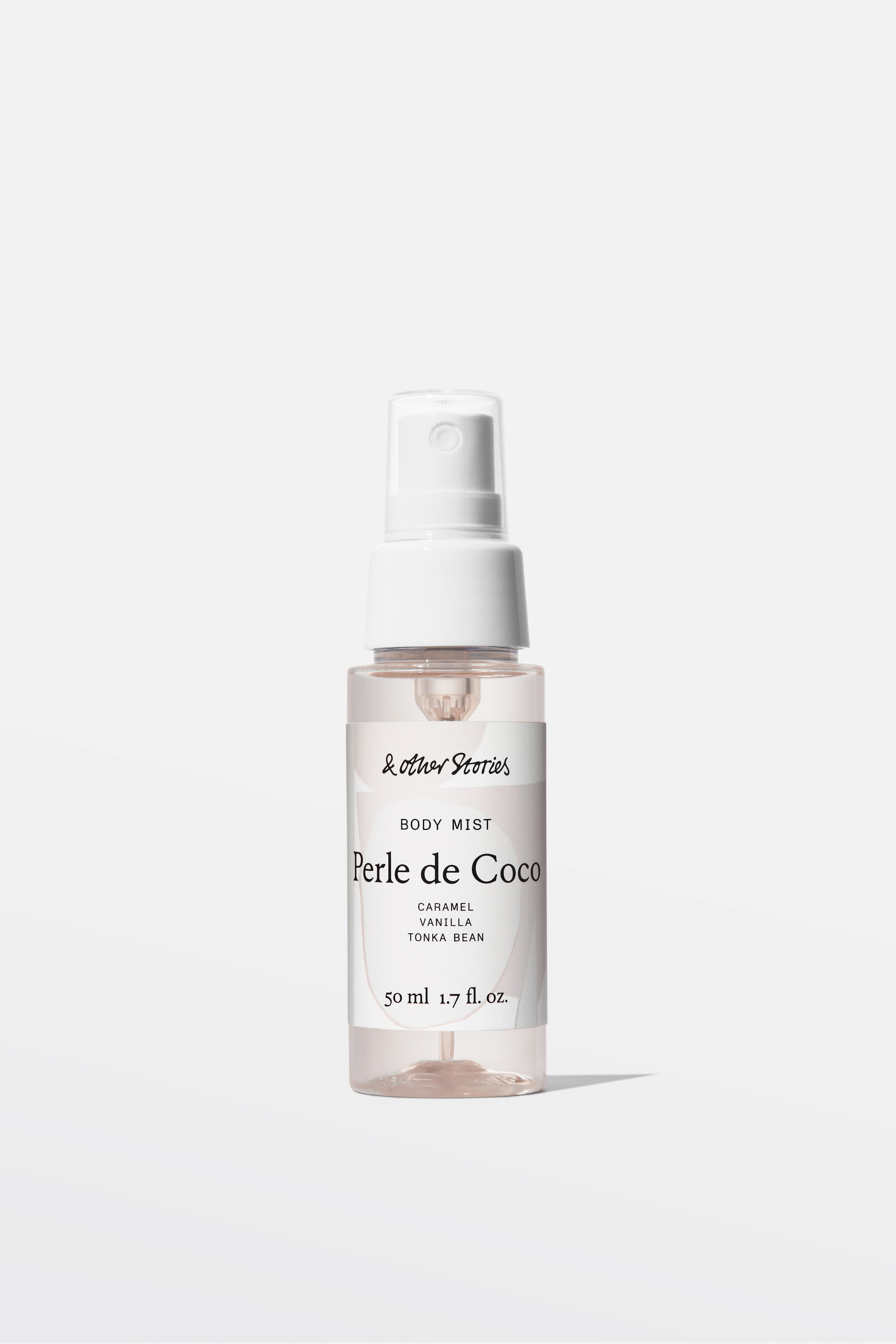Agrandir l'image: Une bouteille de brume corporelle mini, cylindrique et transparente, est posée debout, présentant son devant, contenant un liquide rose clair et surmontée d'une pompe vaporisateur blanche avec un capuchon transparent. Son étiquette blanche affiche "BODY MIST Perle de Coco" avec des notes olfactives de "CARAMEL VANILLE FÈVE TONKA" et "50 ml 1.7 fl. oz."
