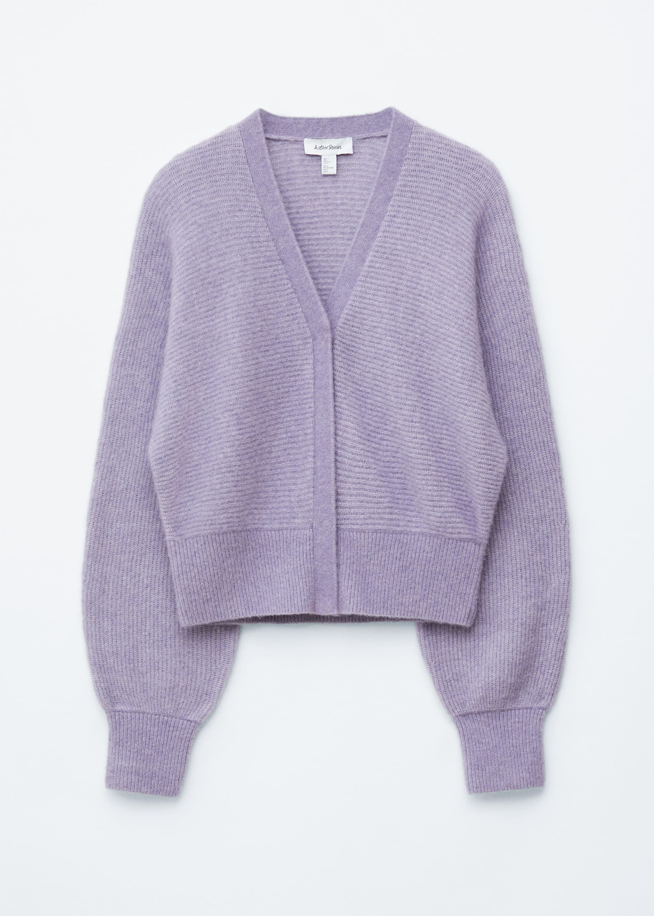 Visualizza immagine più grande: Un cardigan corto di colore viola chiaro è presentato frontalmente, caratterizzato da uno scollo a V e una texture a maglia a coste. Il corpo principale e le maniche lunghe e voluminose presentano costine orizzontali, mentre le maniche hanno polsini a coste verticali e un orlo a coste verticali. Una pattina frontale è visibile.